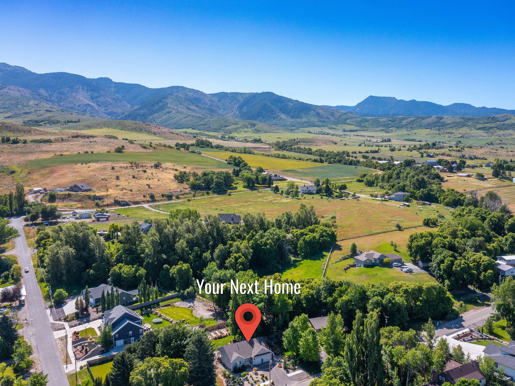 Aerial perspective showcasing the residential area amidst expansive green fields and distant mountains