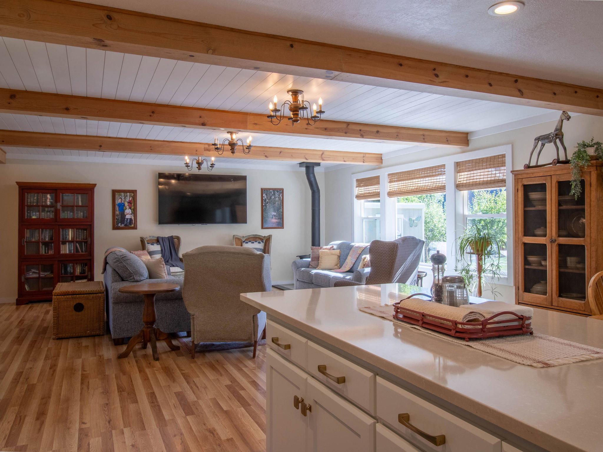 Open-concept living space with exposed wood ceiling beams, shiplap ceiling accents, wood-finish flooring, and multiple windows