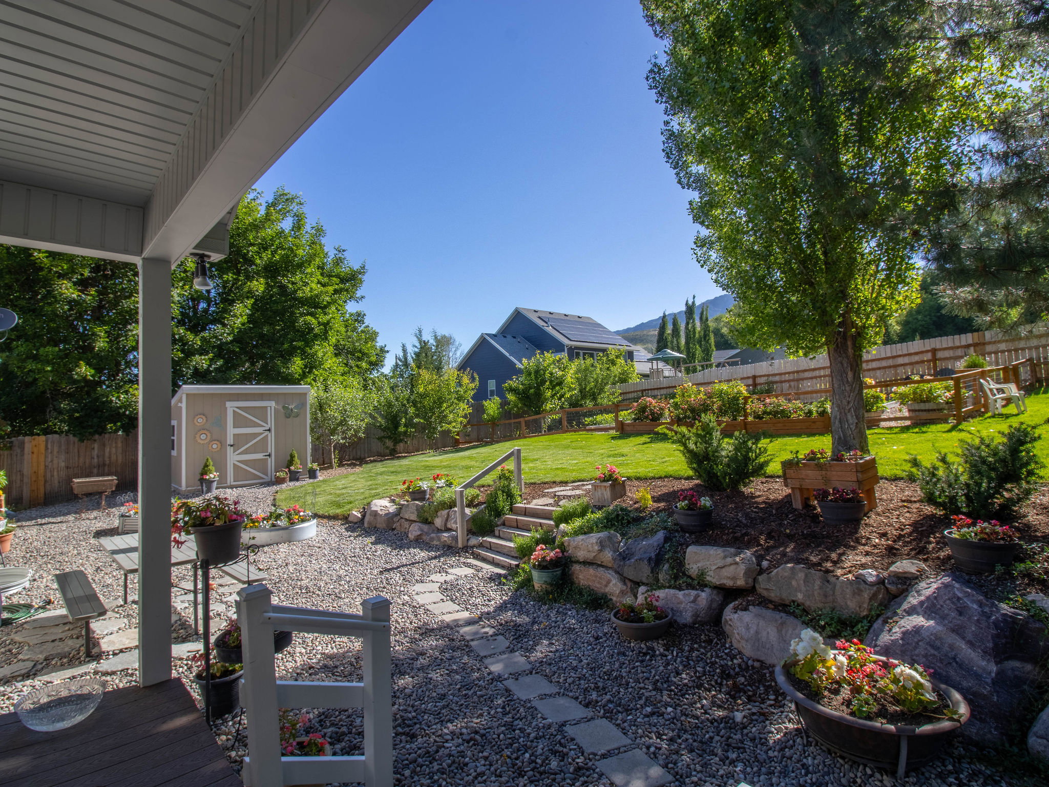 Multi-tiered backyard featuring a covered patio, gravel hardscaping with stepping stones, a rock retaining wall, and a sloped lawn area