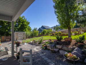 Multi-tiered backyard featuring a covered patio, gravel hardscaping with stepping stones, a rock retaining wall, and a sloped lawn area