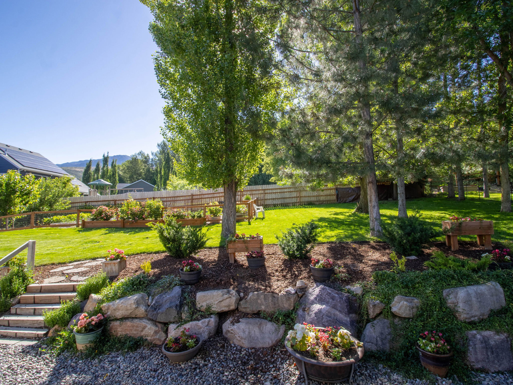 Tiered backyard featuring a stone retaining wall, gravel patio, and stone steps