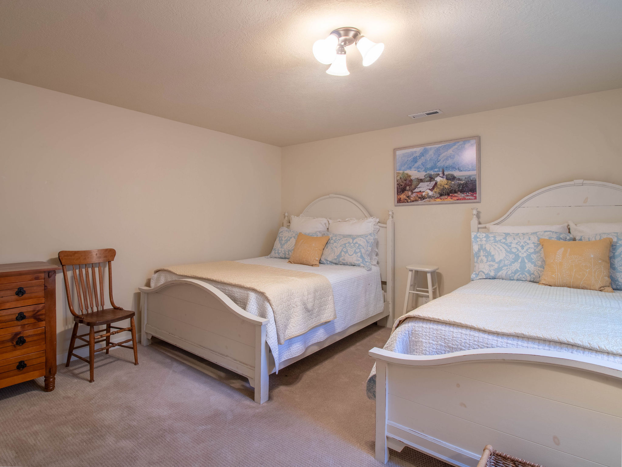 Carpeted room with neutral walls, featuring two white-framed beds with headboards and footboards
