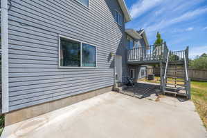 Multi-level exterior featuring gray horizontal siding, a concrete patio, and an elevated wood deck with stairs to the yard