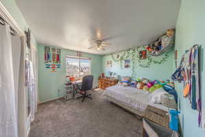 Bedroom featuring a ceiling fan, window with exterior views, light-colored walls, and gray carpet flooring