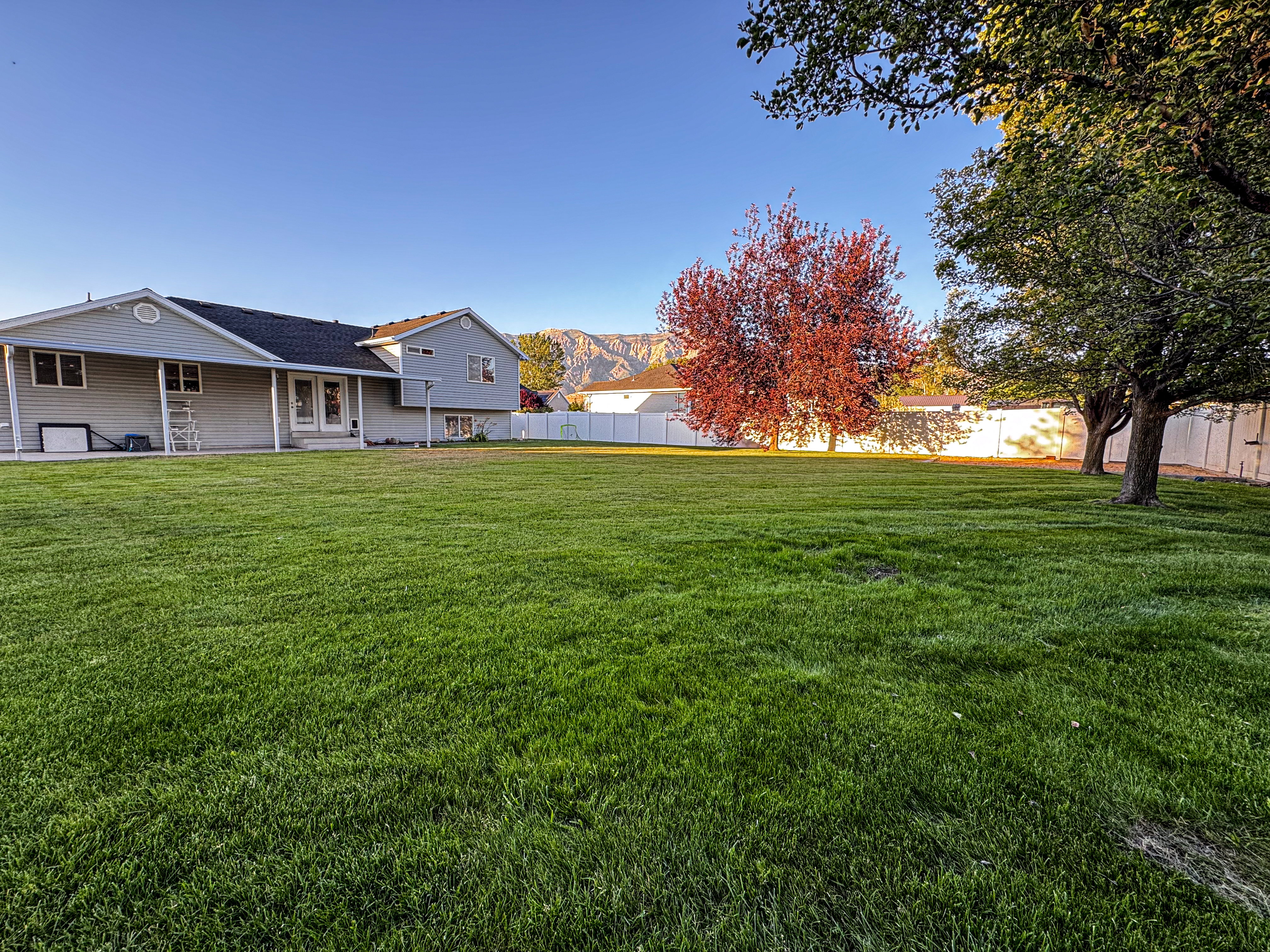 Expansive green lawn with mature trees and a white privacy fence, featuring a backdrop of distant mountains