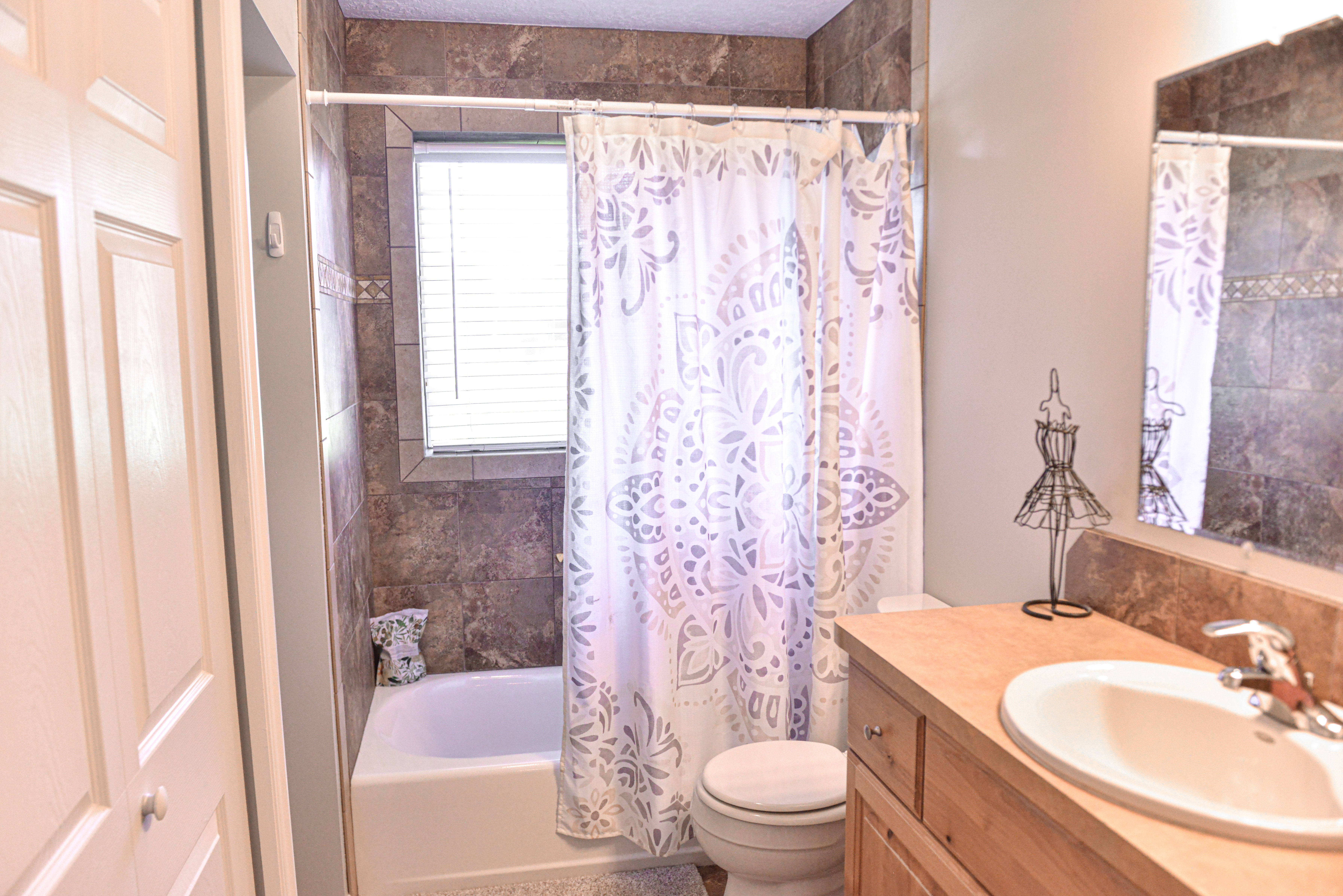Bathroom featuring a tub/shower combination with full-height tile surround and a window with blinds