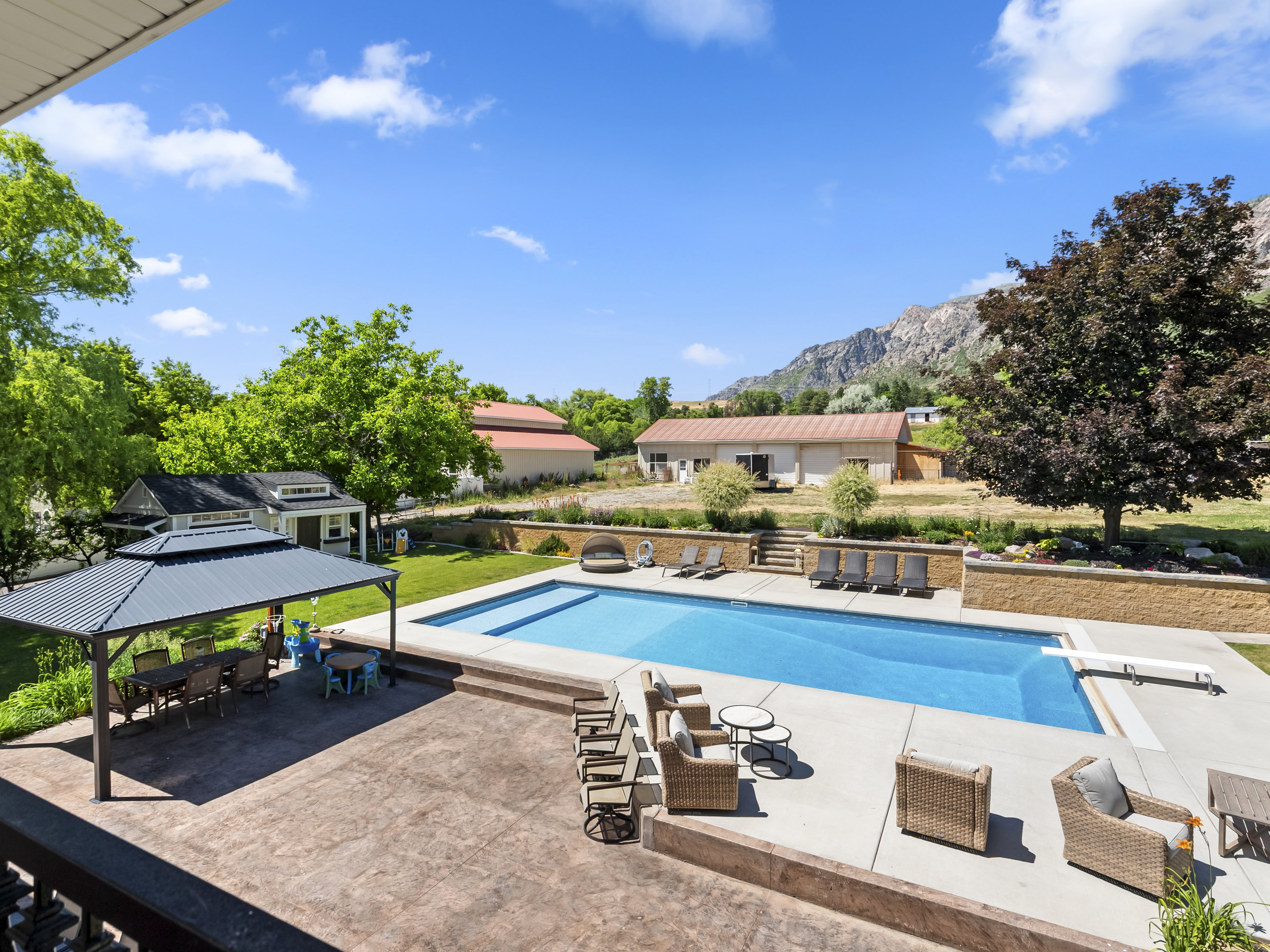 Expansive backyard featuring a rectangular swimming pool with diving board, a large stamped concrete patio, a built-in gazebo, and terraced landscaping with retaining walls