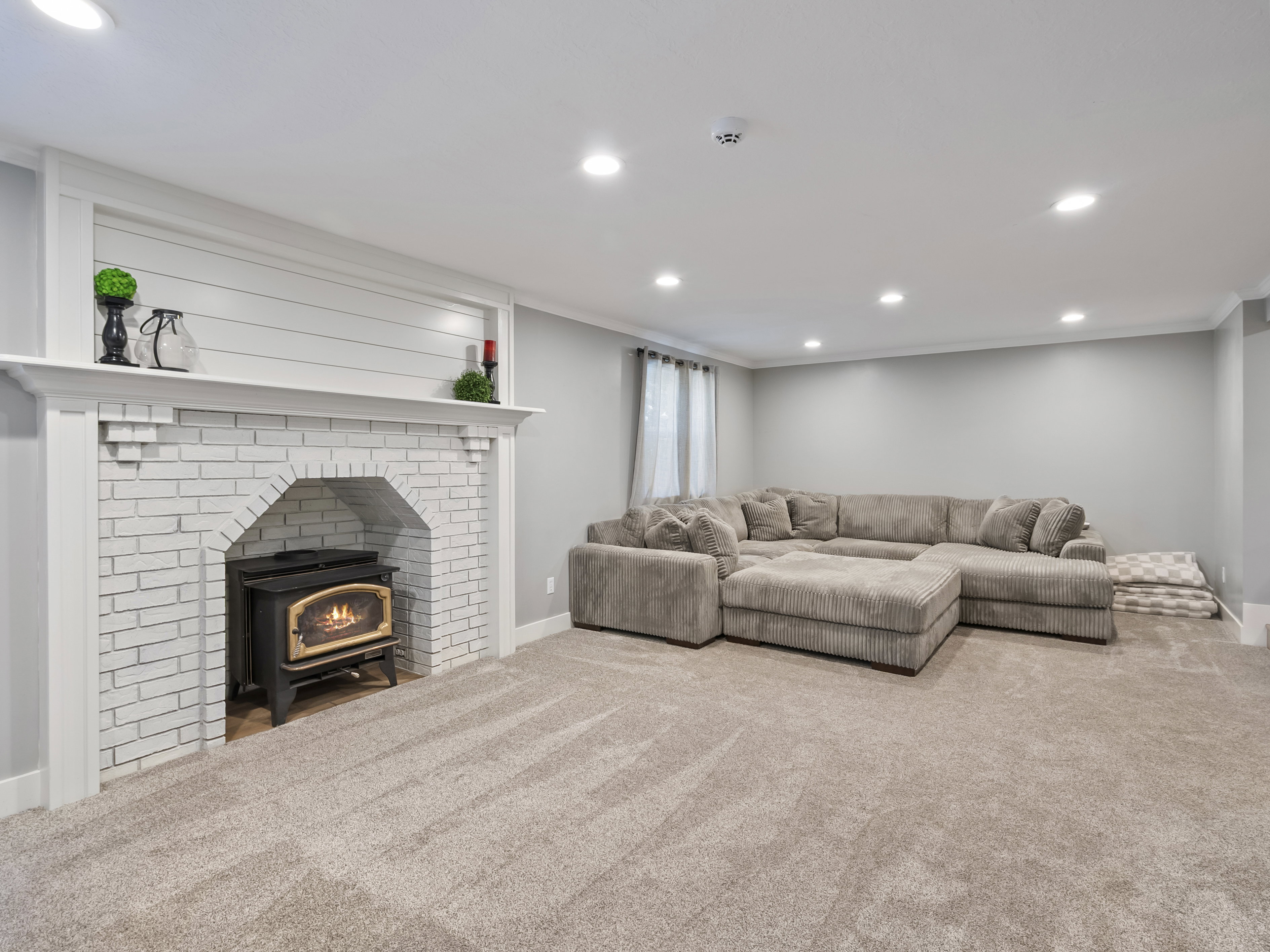 Finished lower level featuring a white painted brick fireplace with a wood-burning stove insert, shiplap detailing, and recessed lighting