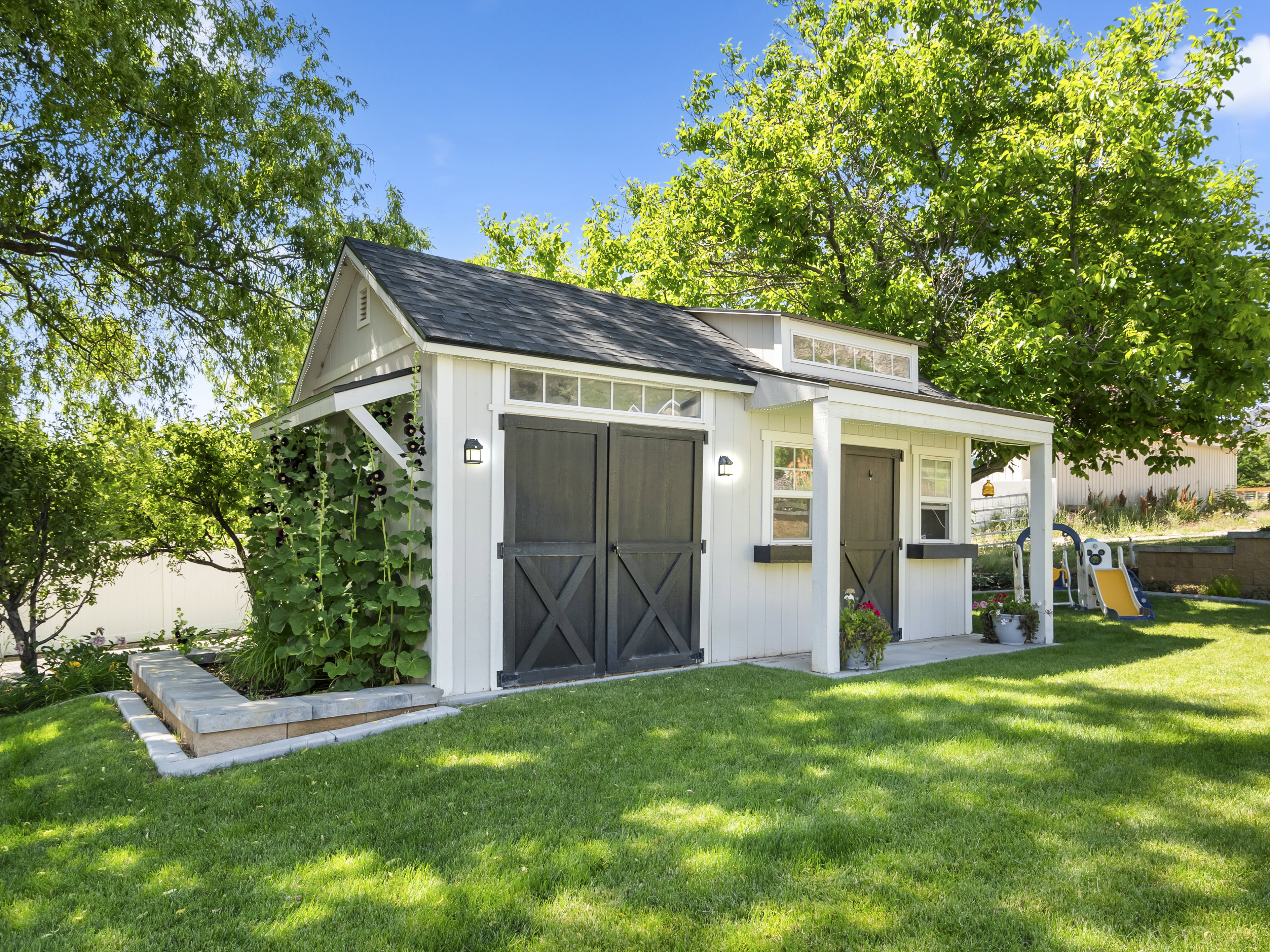 White-sided shed with dark barn doors, a covered porch, and a raised garden bed
