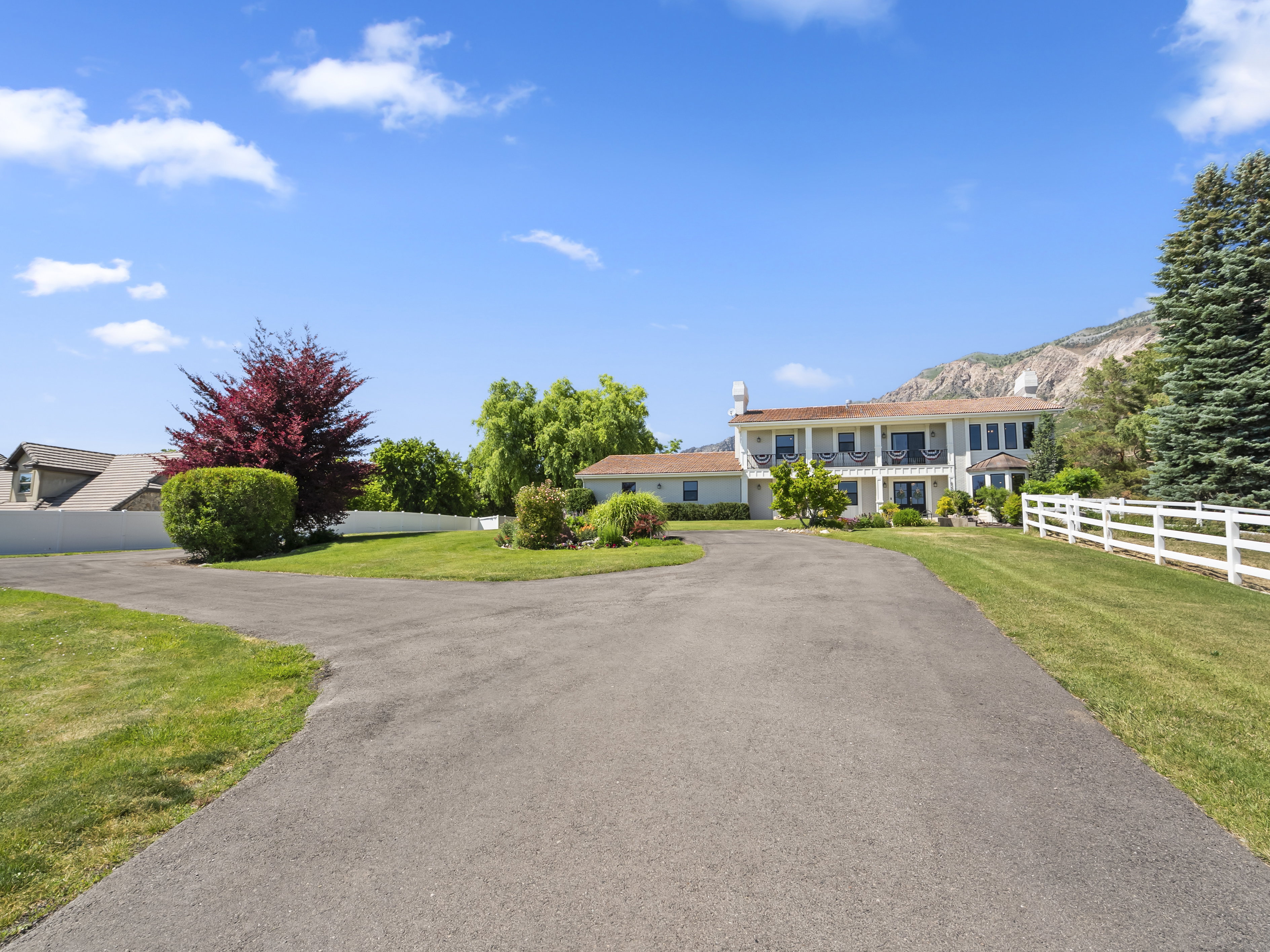 Paved driveway leading to a multi-level residence with a white post-and-rail fence