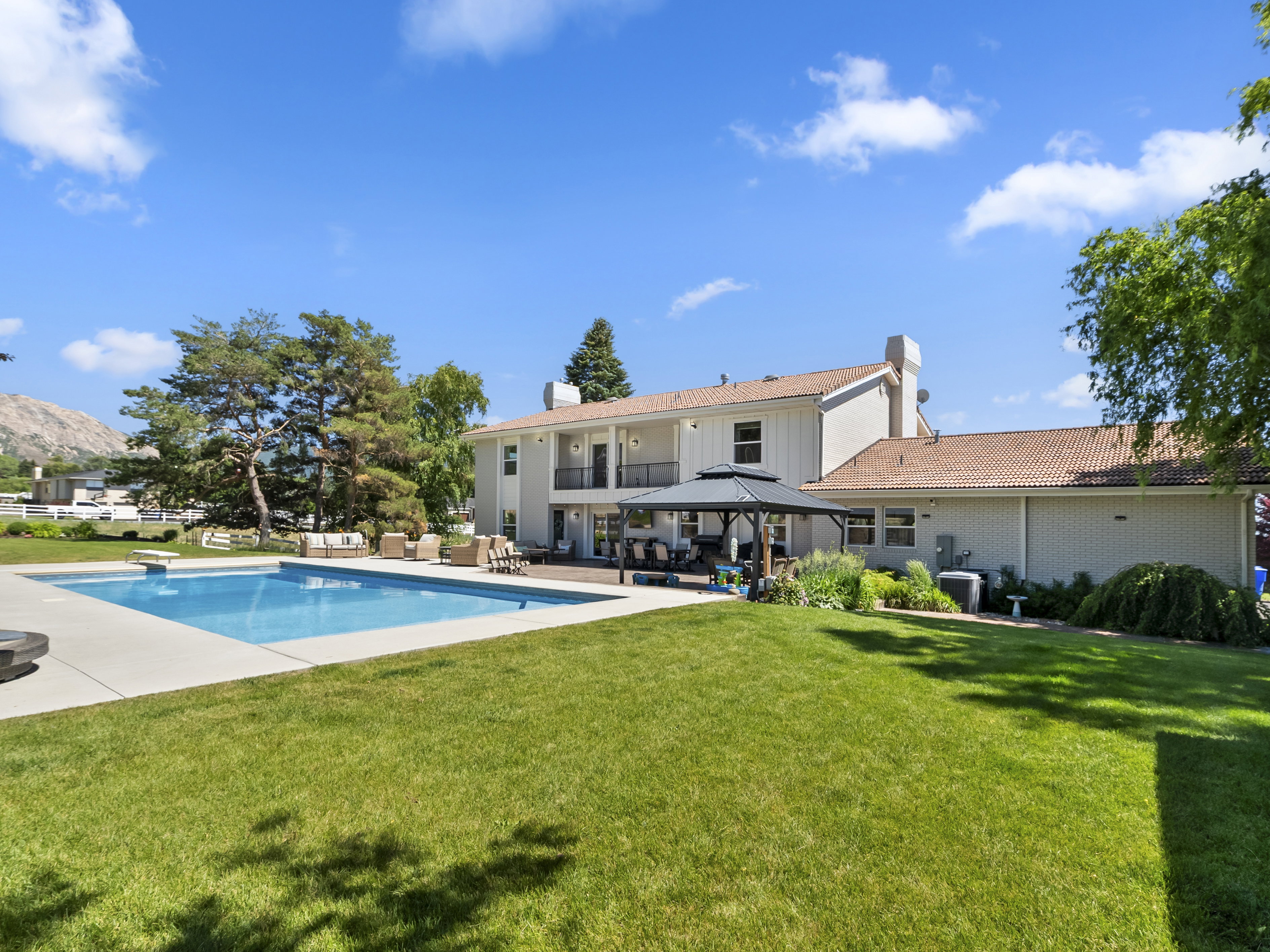 Expansive backyard featuring an in-ground pool with a diving board, surrounding concrete patio, and a covered gazebo