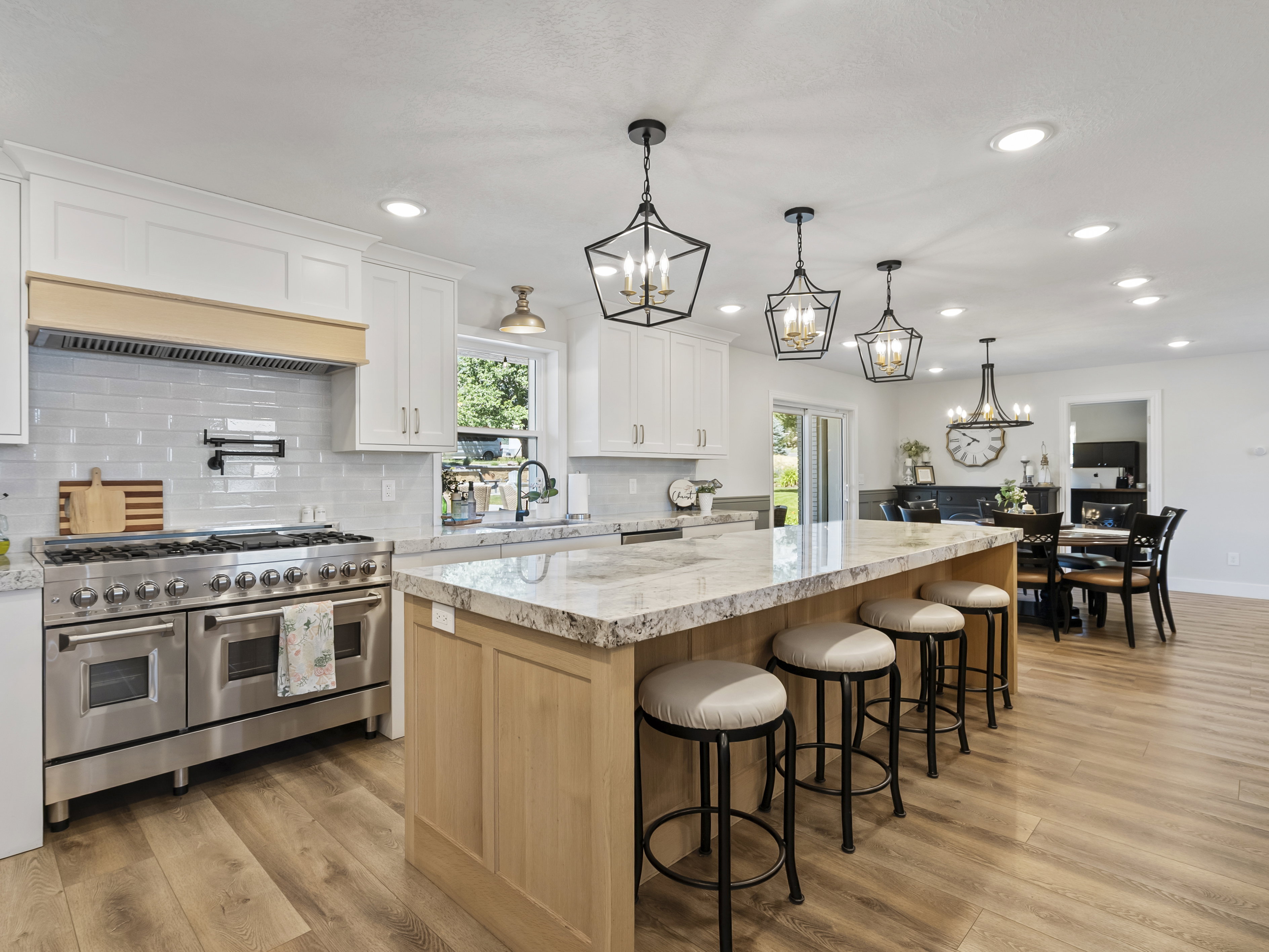 Open-concept kitchen featuring an expansive island with seating, stainless steel professional-grade range, light-toned wood-finish flooring, white shaker cabinetry, and recessed lighting