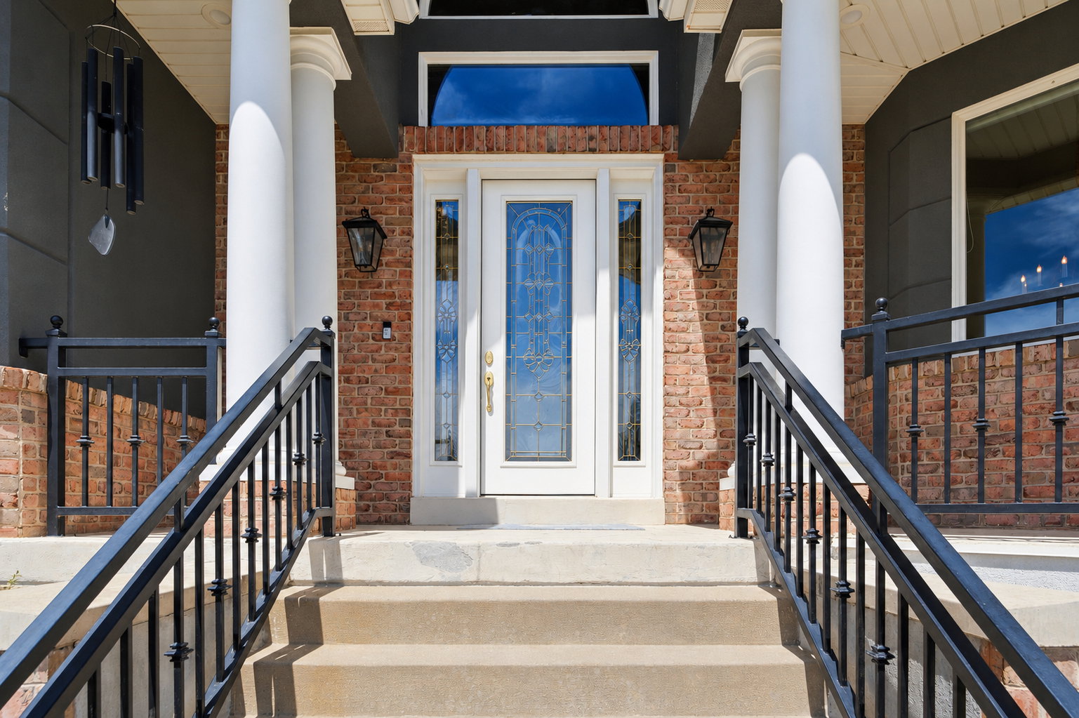 Inviting front entrance featuring a brick facade, white columns, decorative entry door with leaded glass, concrete steps, and black metal railings