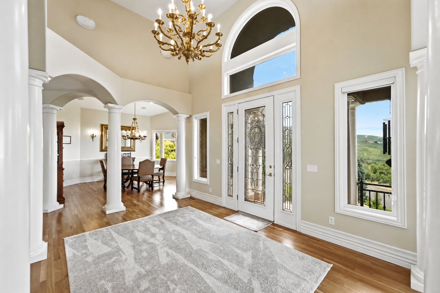 Grand entryway featuring double doors with decorative glass, an arched transom window, and a brass chandelier