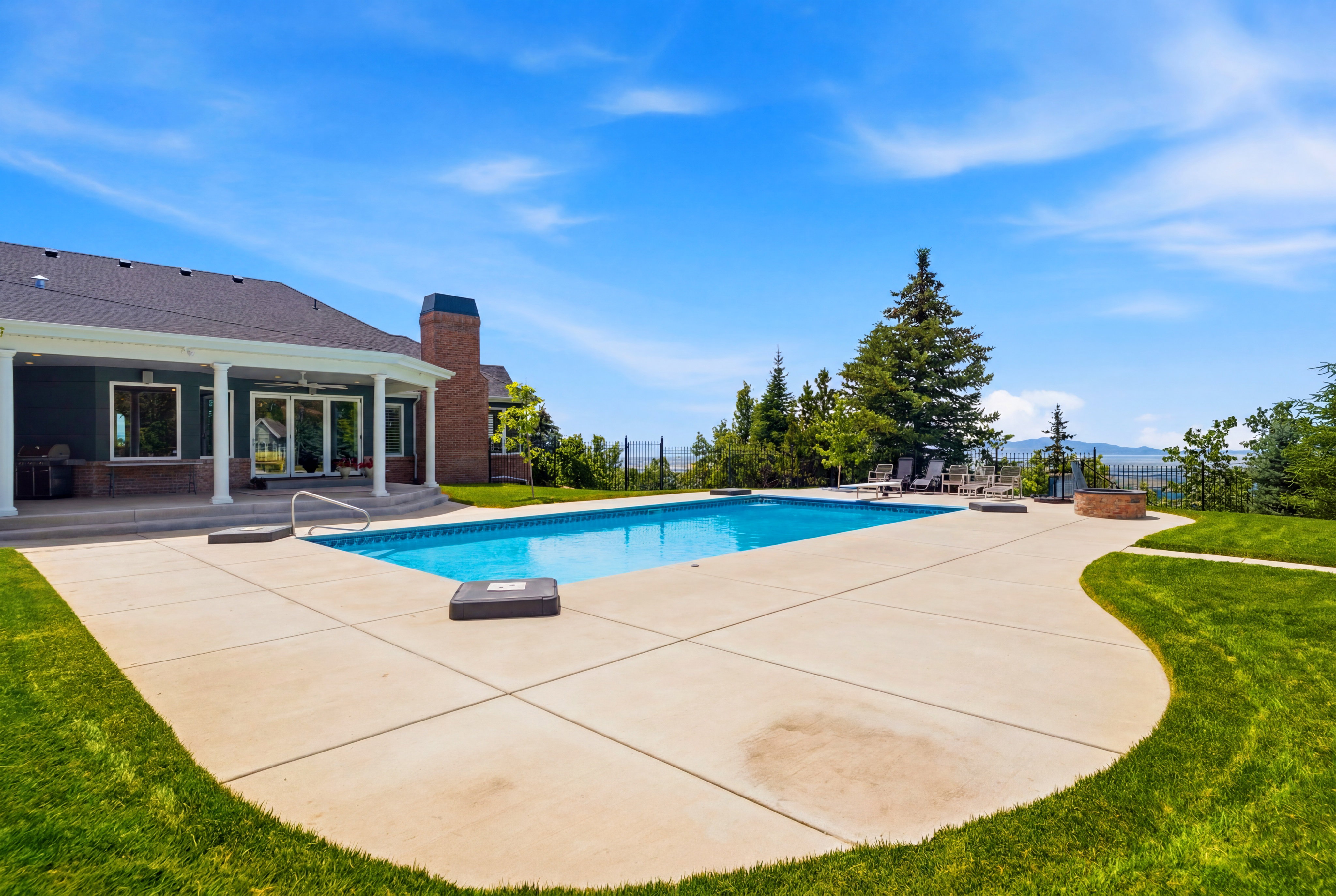 Expansive outdoor living area featuring a rectangular swimming pool, concrete patio surfacing, and manicured lawn