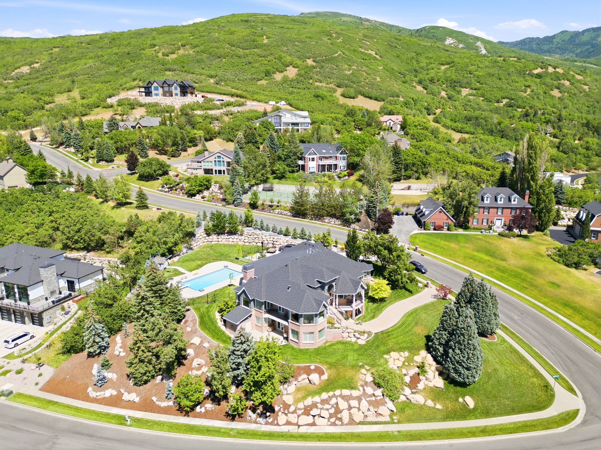 Expansive property featuring a large residence with a dark shingle roof, surrounded by mature trees and manicured landscaping