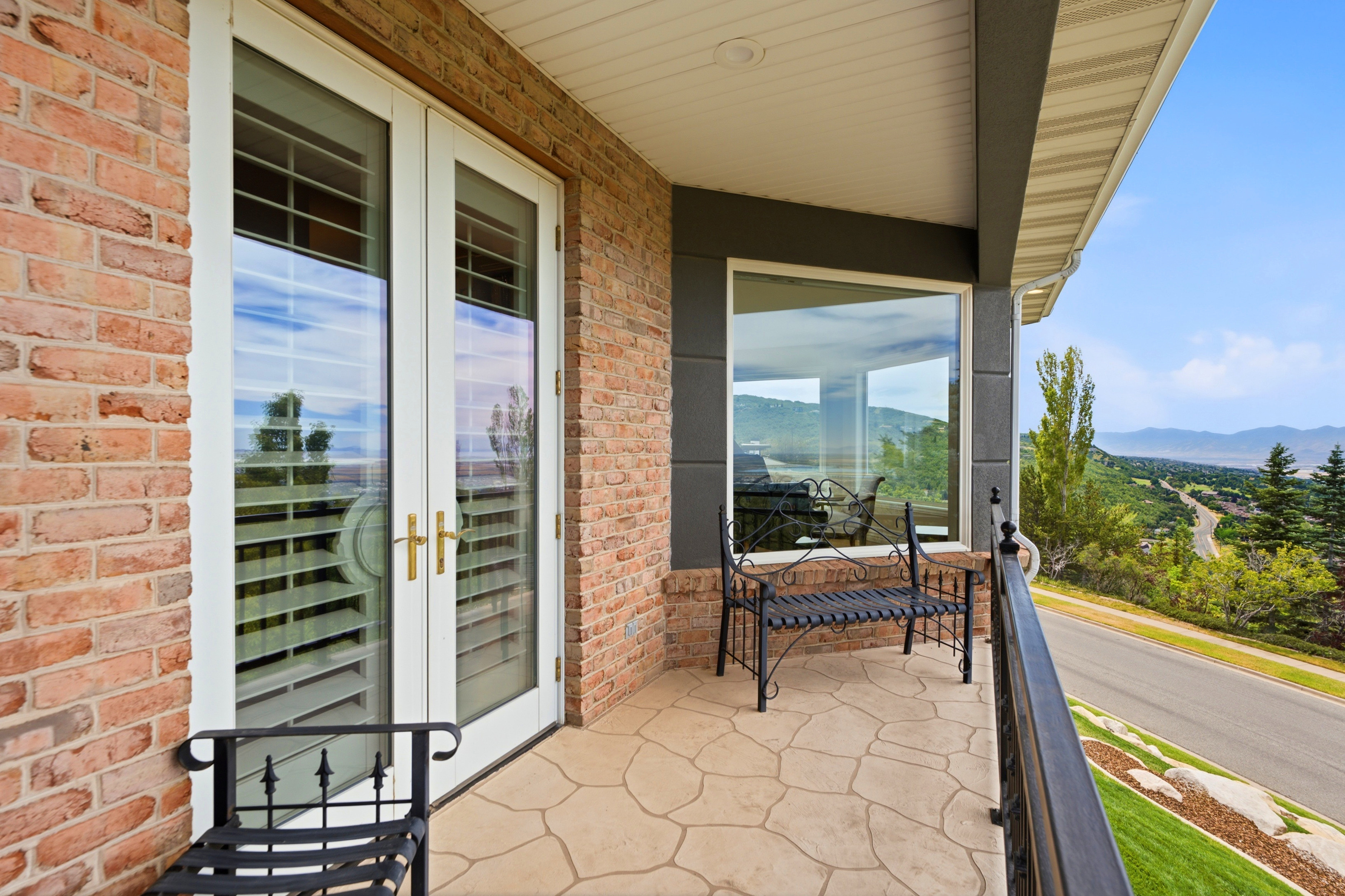 Front patio balcony featuring French doors with internal blinds, brick siding, a stamped concrete surface, an exterior window, and a metal railing