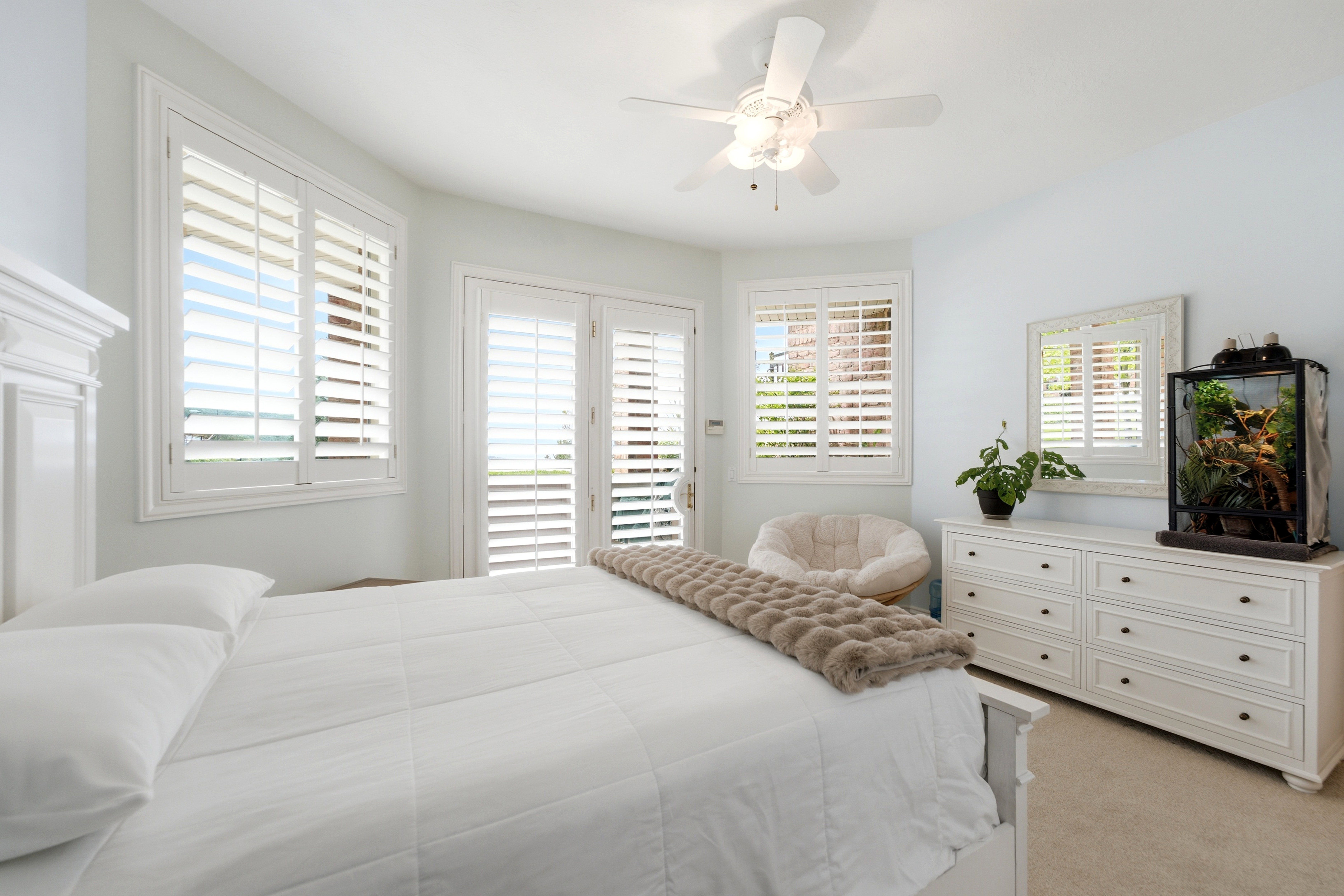 One of three Bedrooms.  Spacious bedroom featuring multiple windows with louvered shutters, walk out balcony, a white ceiling fan, and carpeted flooring