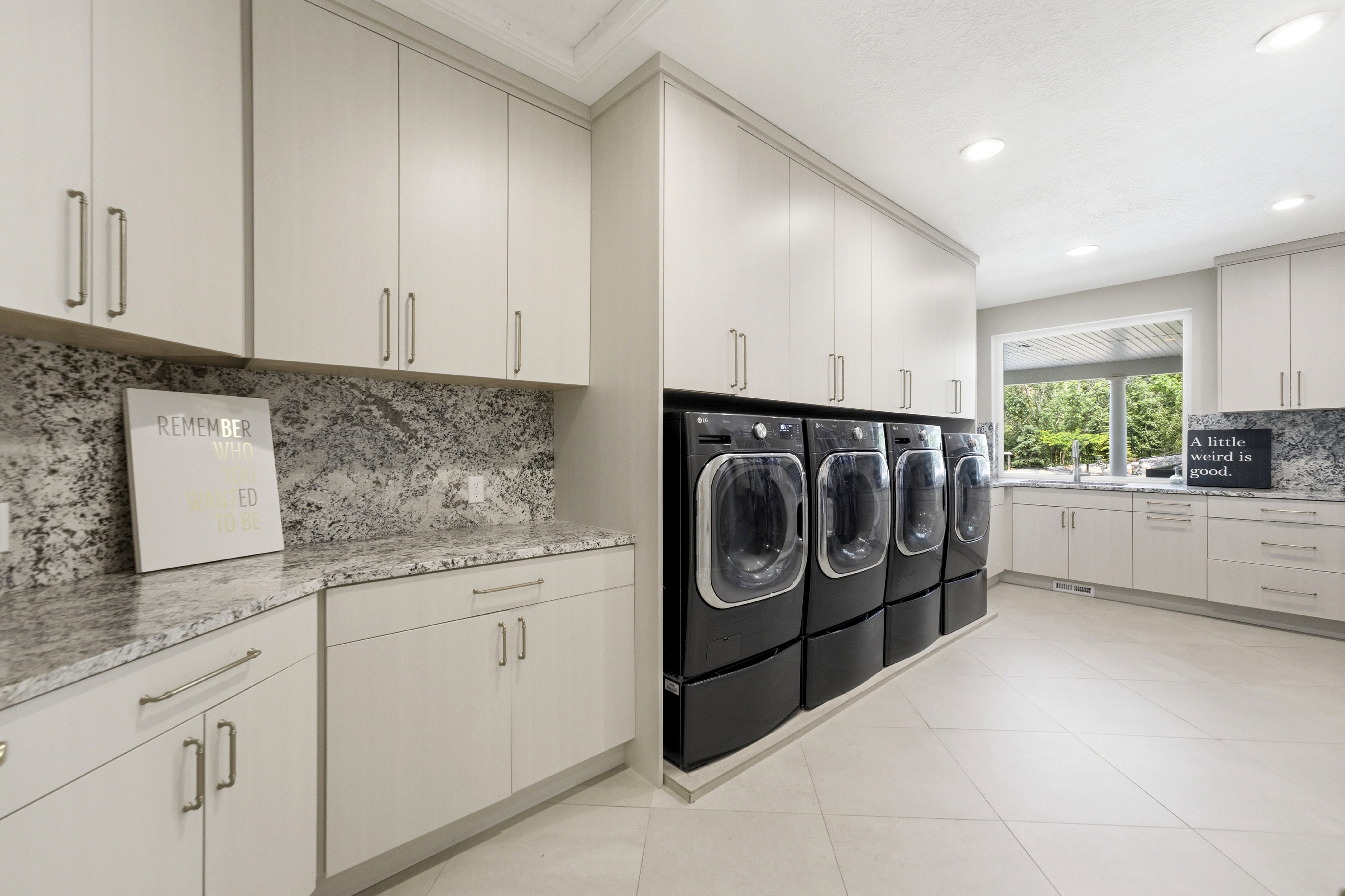 Spacious utility room featuring extensive light cabinetry, contrasting dark front-loading laundry appliances, and ample countertop space with a matching backsplash