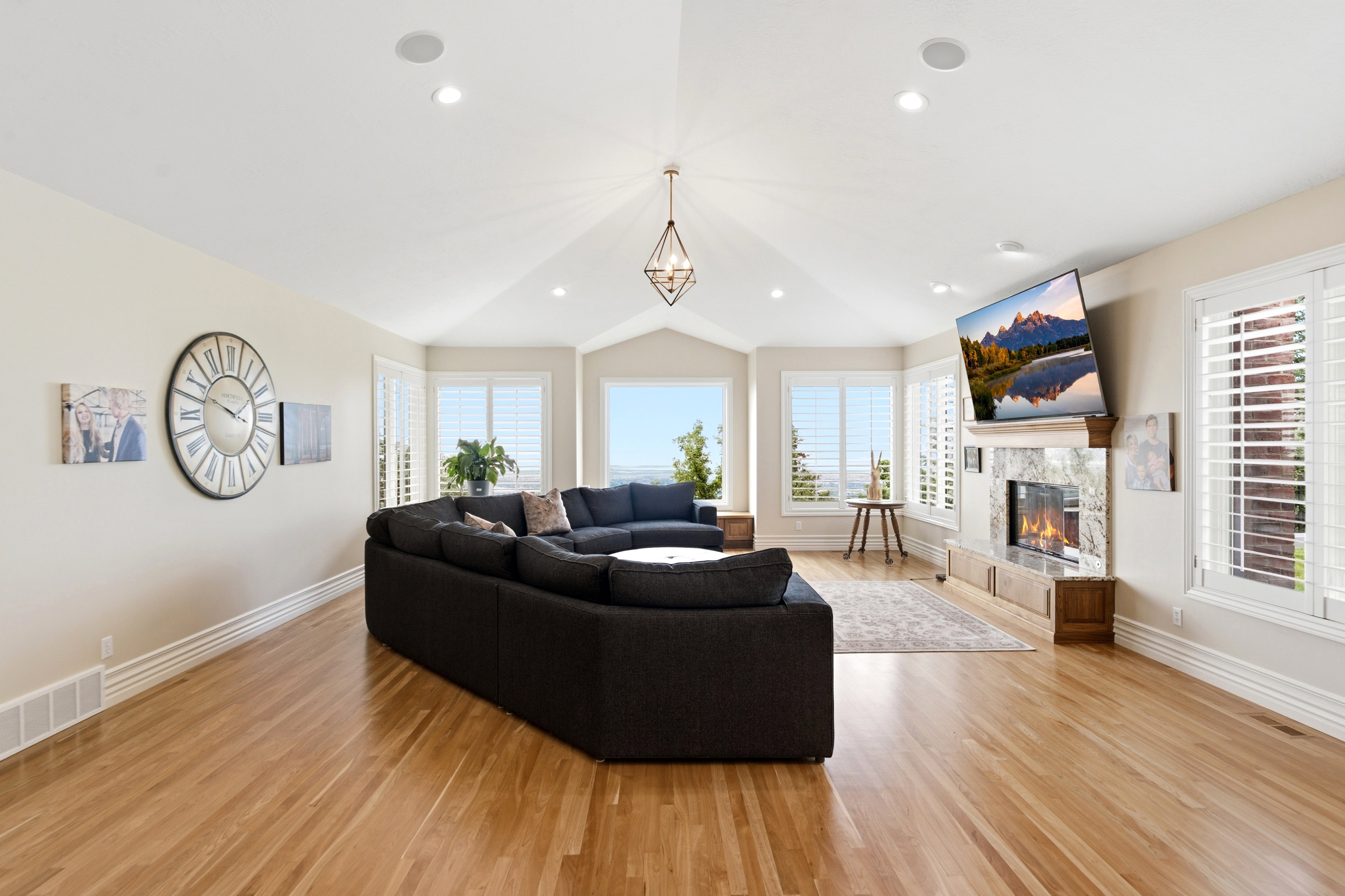 Living area with wood-finish flooring, vaulted ceiling, recessed lighting, and a prominent fireplace with a stone surround and wood mantle