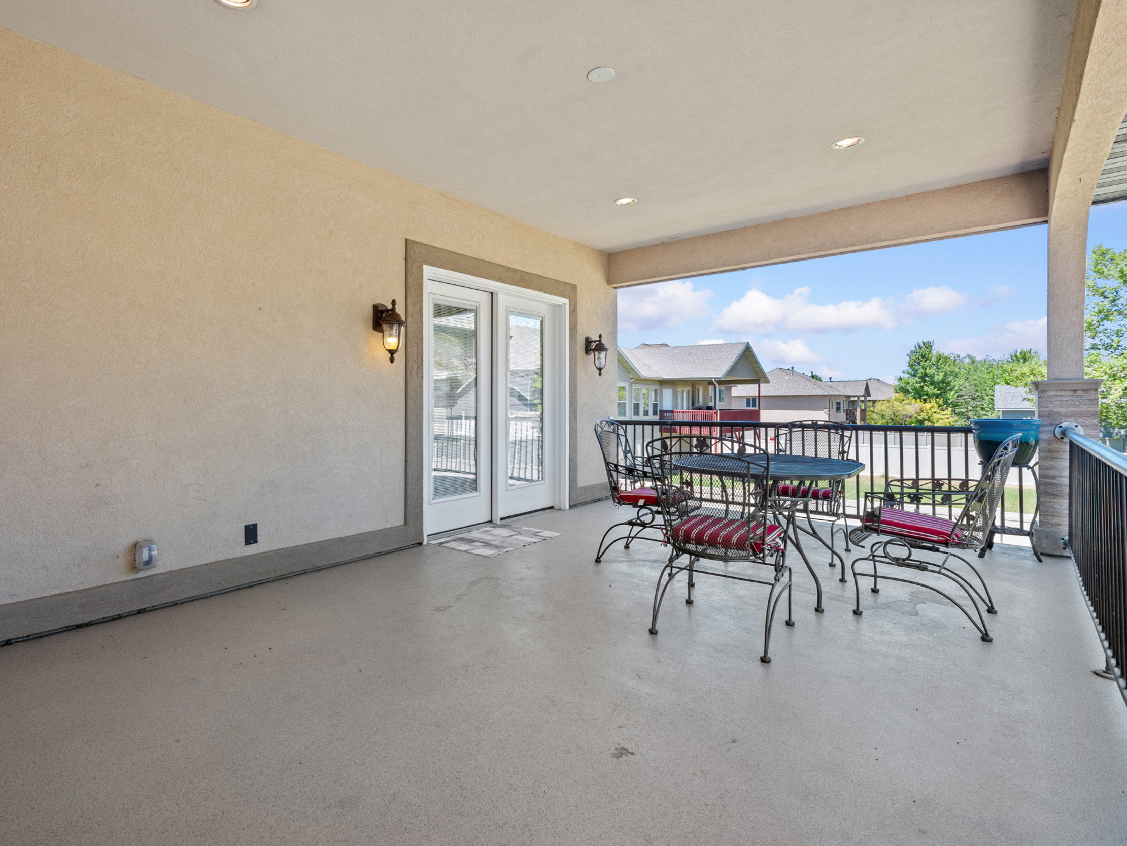 Spacious covered outdoor patio featuring a neutral stucco exterior, recessed lighting, and a durable concrete floor