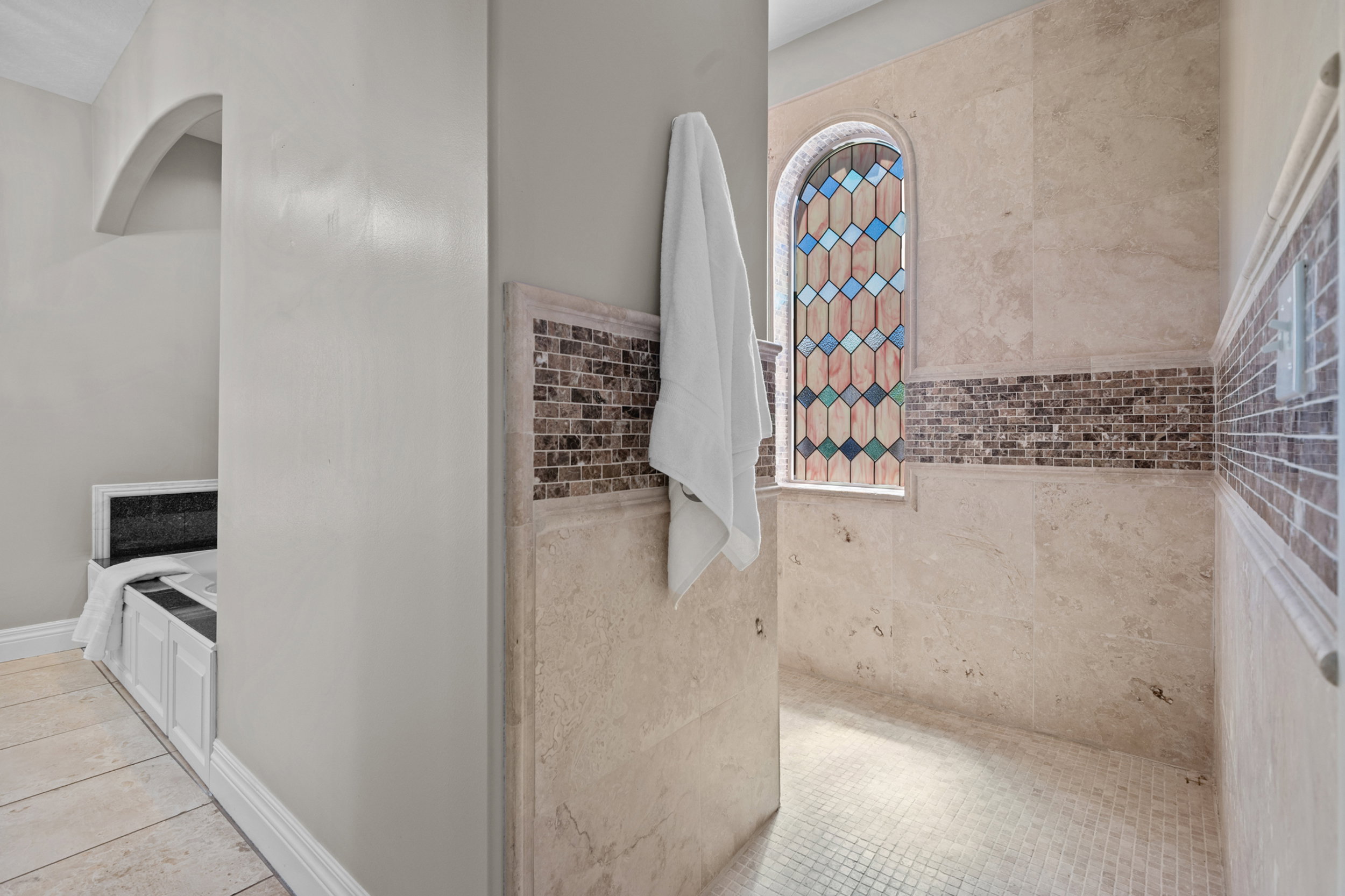 Arched stained glass window above a tiled shower enclosure featuring a mosaic tile accent band
