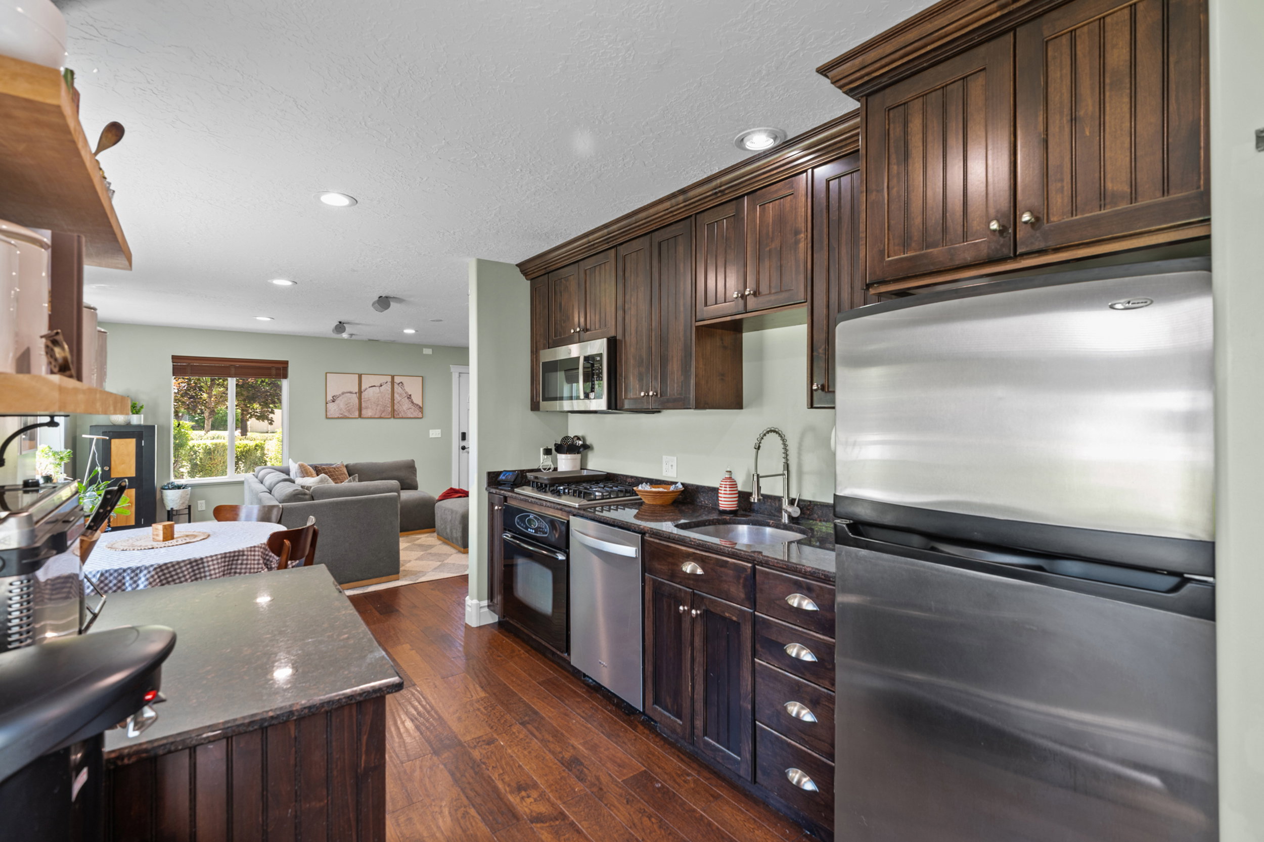 Kitchen featuring dark wood cabinetry, stainless steel appliances, dark countertops, and wood-finish flooring