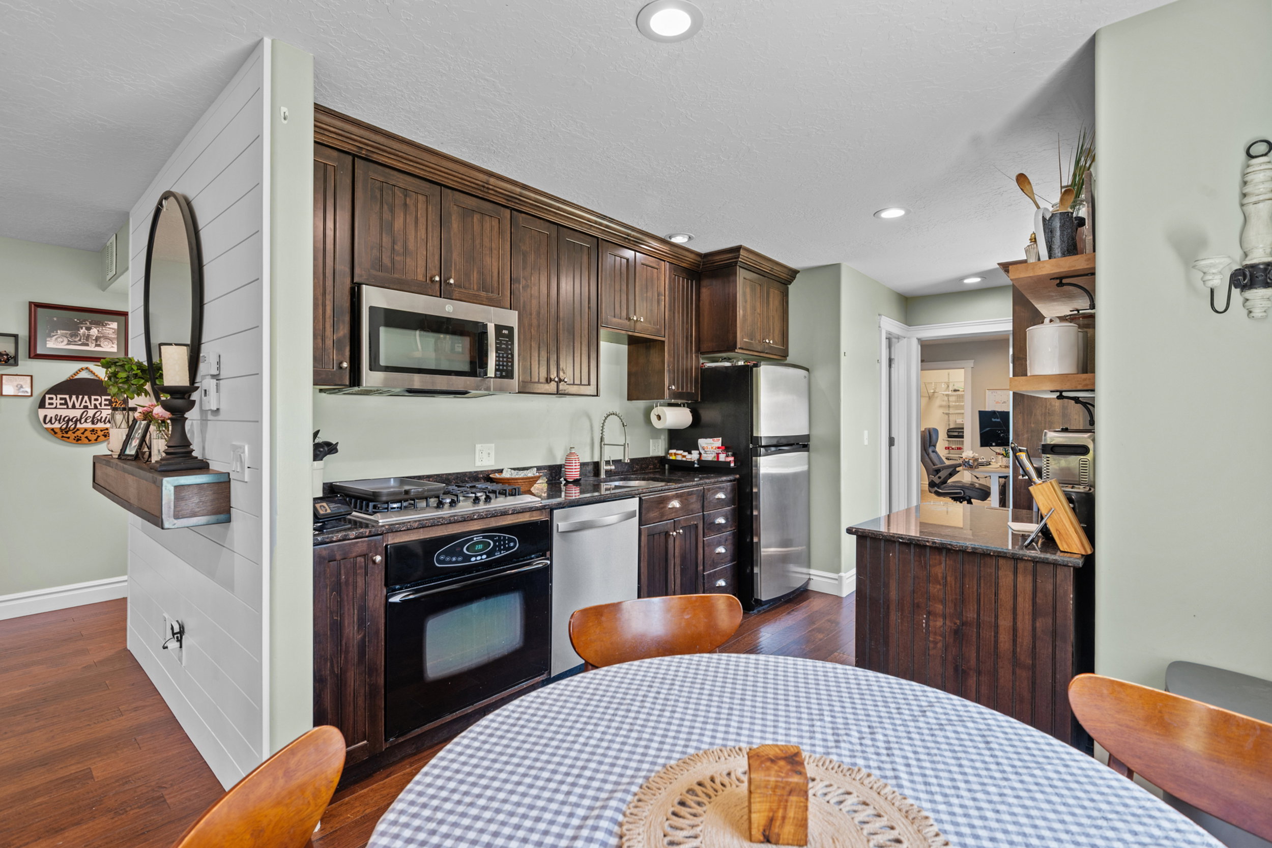Kitchen featuring rich wood cabinetry, stainless steel appliances, dark stone countertops, wood-finish flooring, and recessed lighting