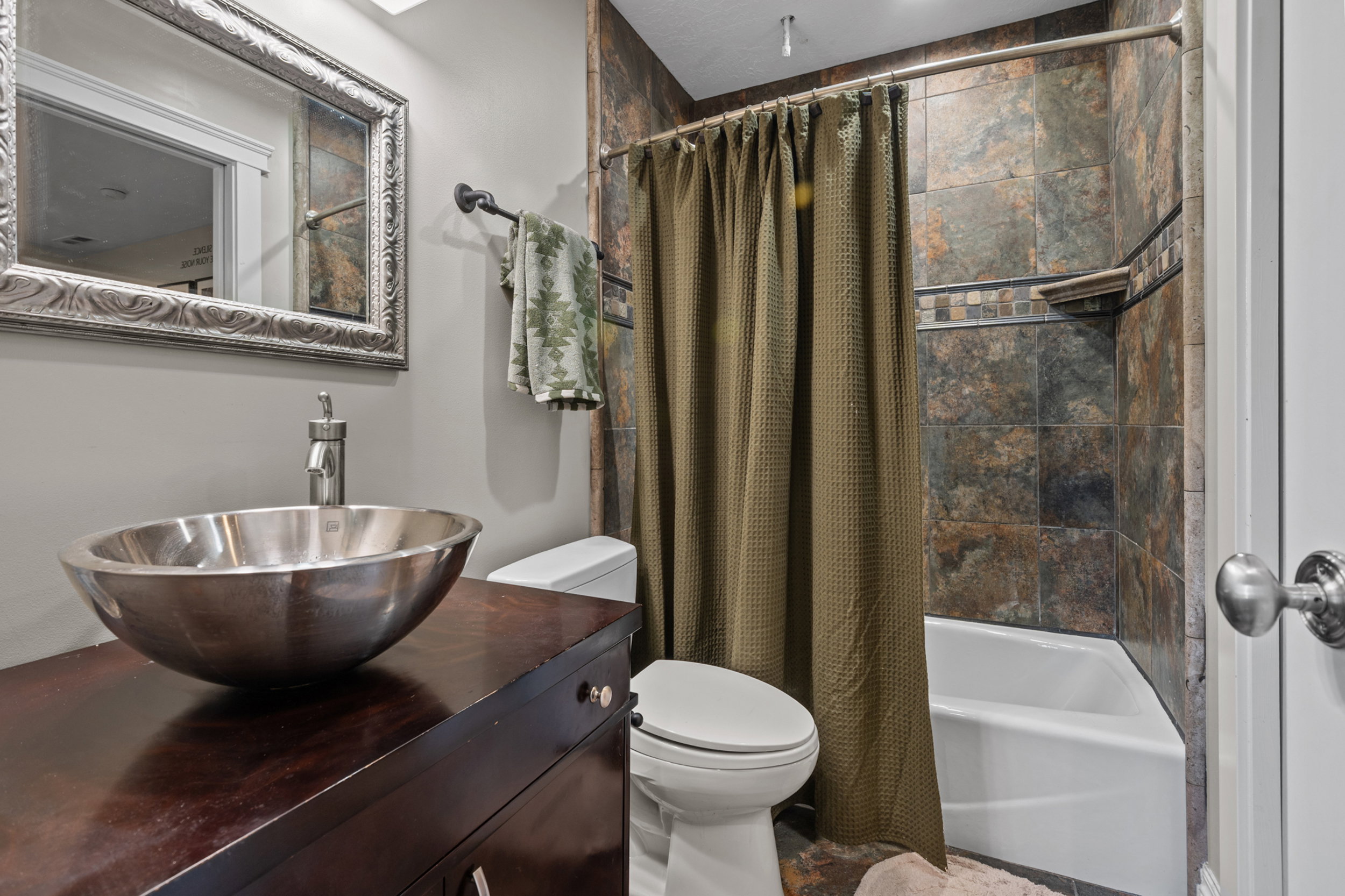 Bathroom featuring a vessel sink, dark wood vanity, and a tub-shower combination with natural stone-look tile surround