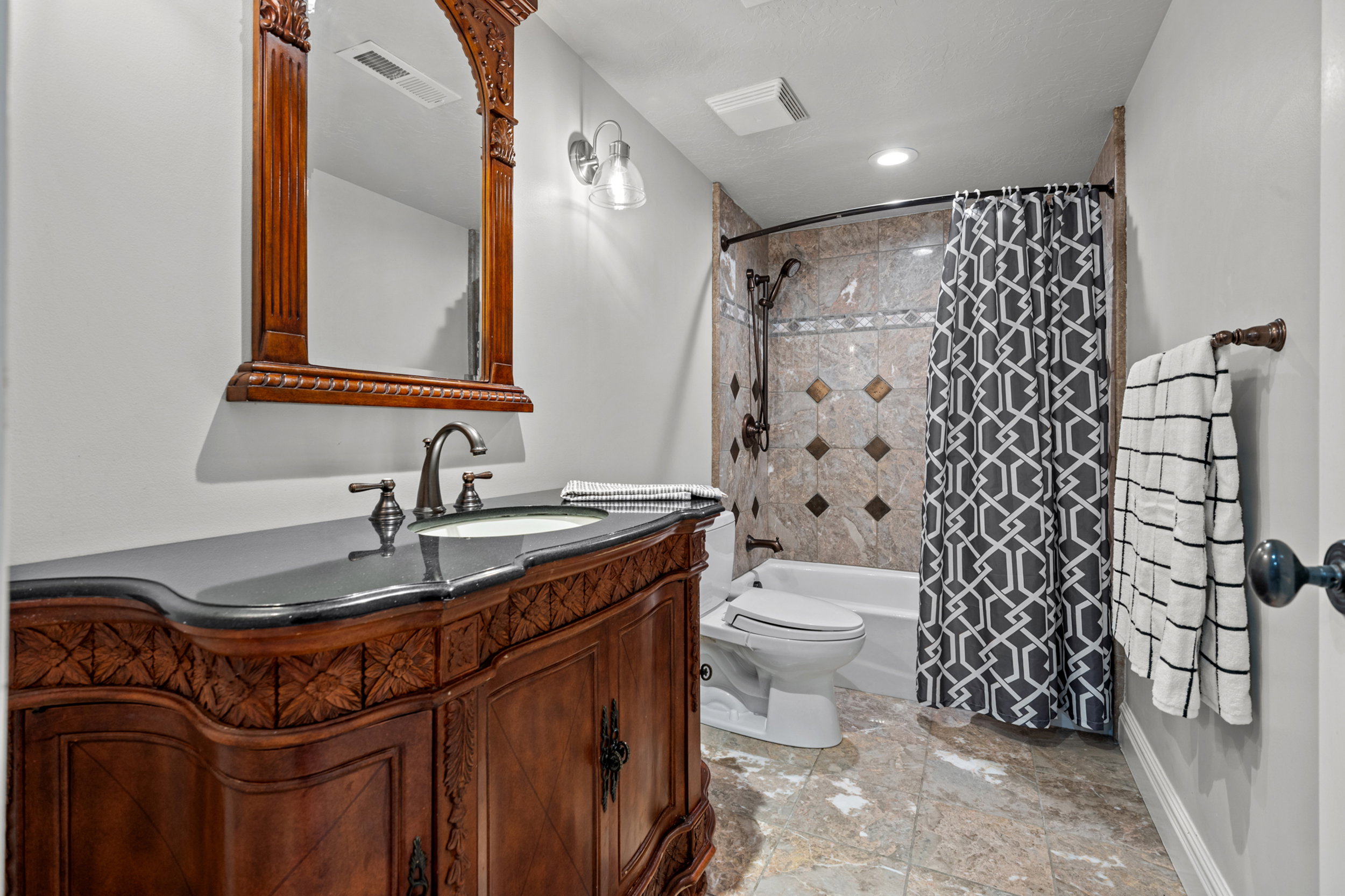Carved wood vanity with a dark countertop and integrated sink, complemented by a decorative framed mirror