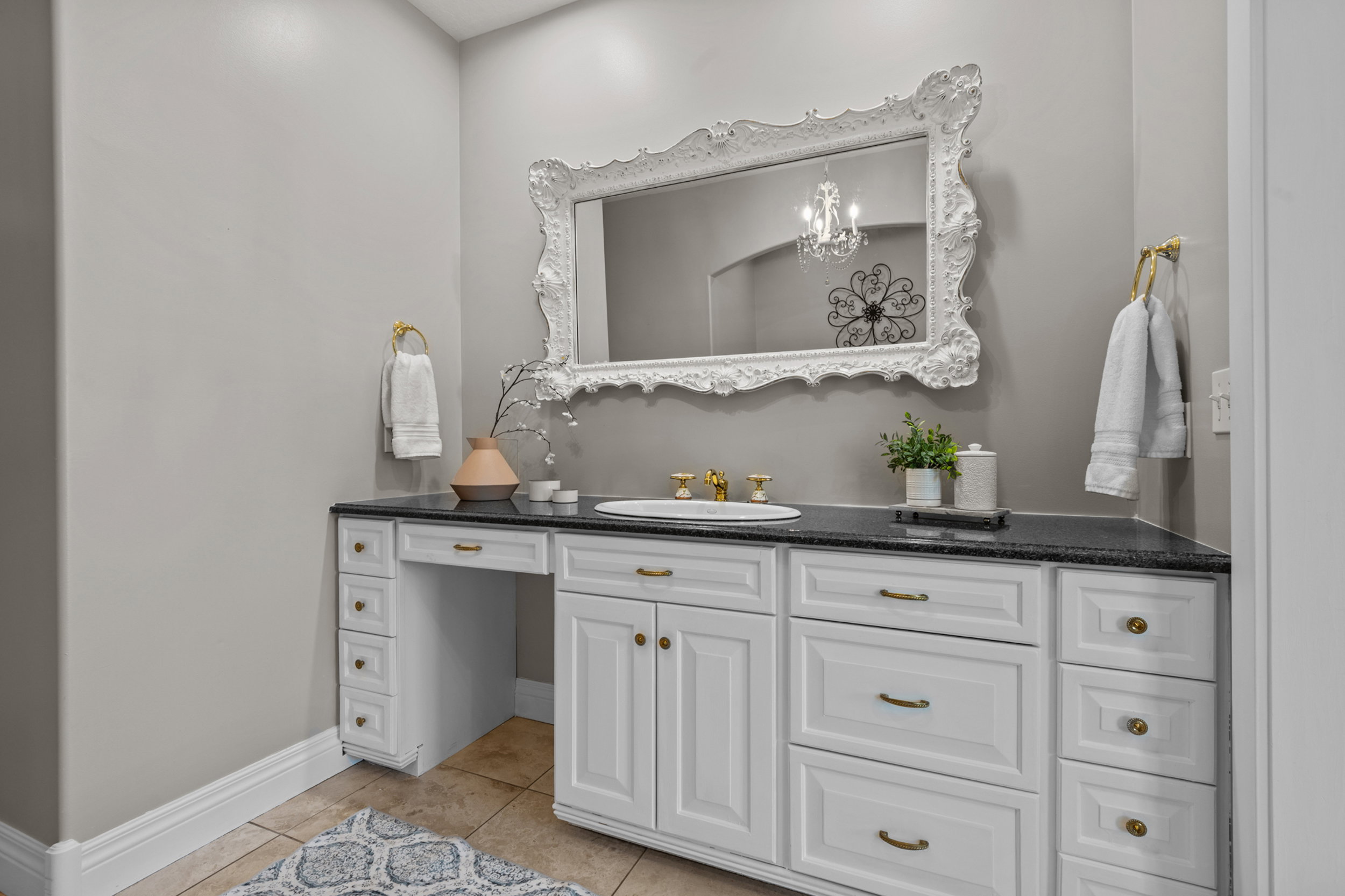White vanity with dark stone countertop, an integrated sink, and an ornate framed mirror