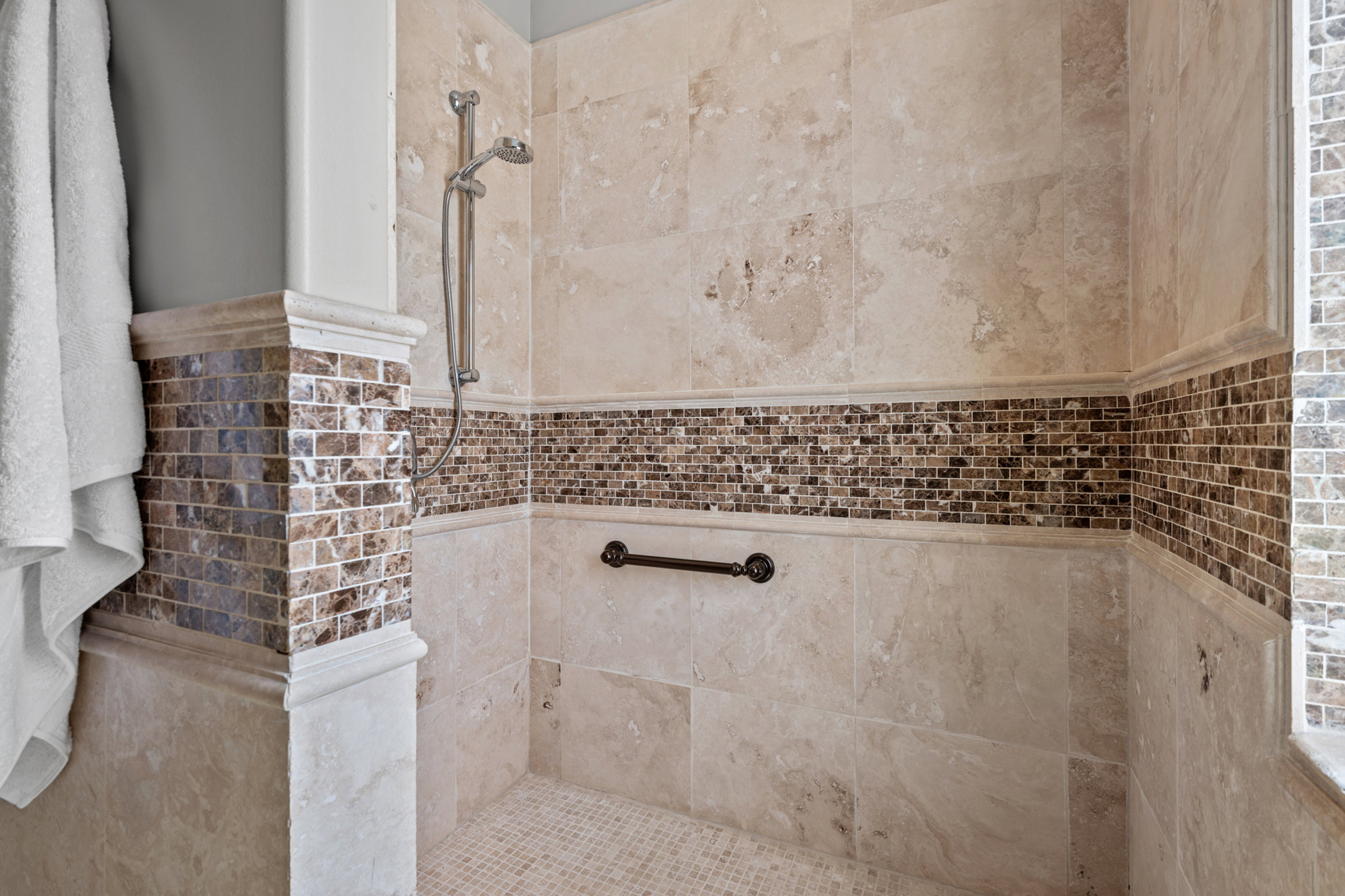 Roll-in shower featuring large format stone tile walls with a decorative mosaic tile accent band
