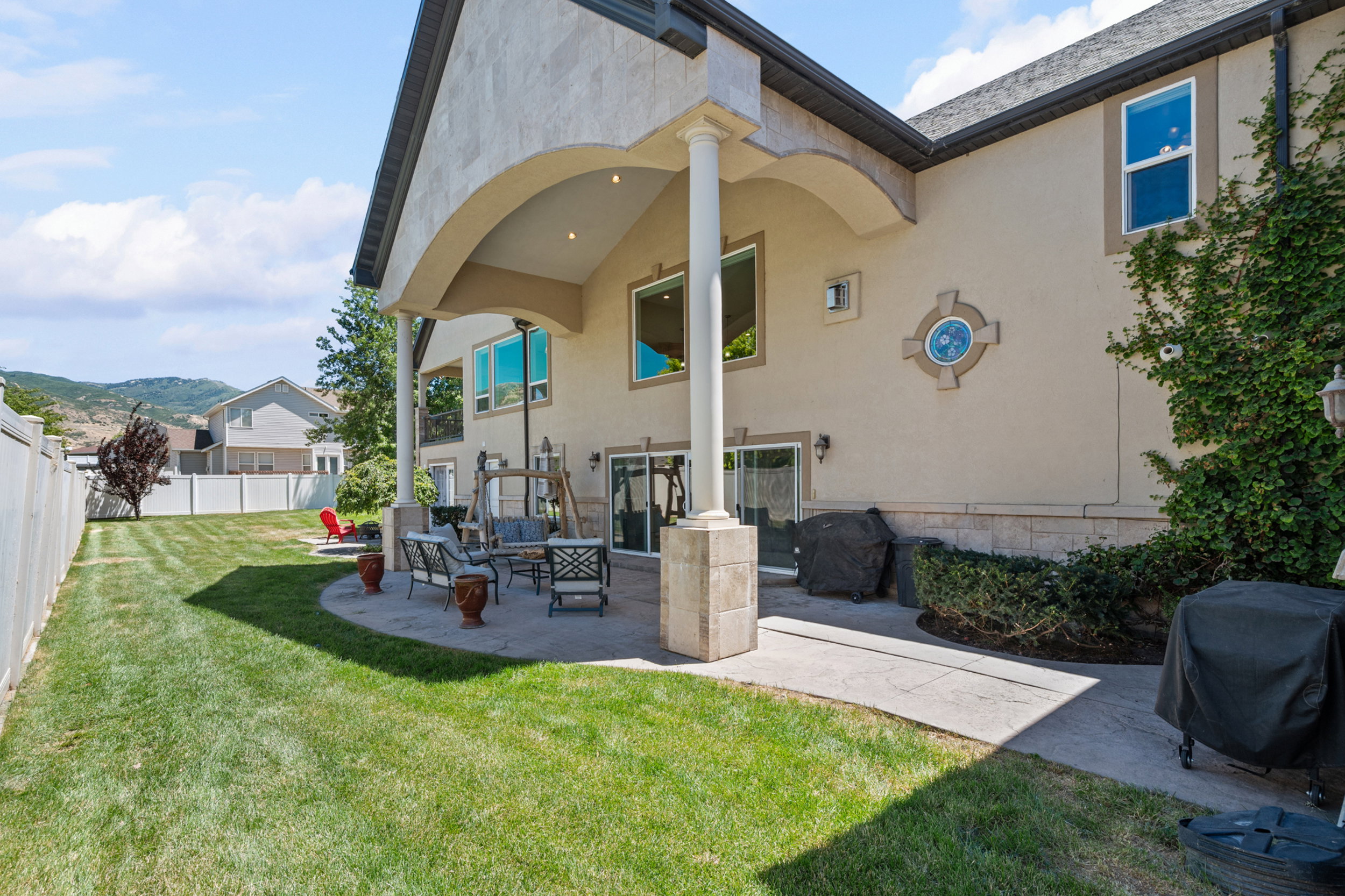 Expansive rear patio featuring a covered seating area with recessed lighting, an arched stucco overhang, and substantial stone-clad pillars