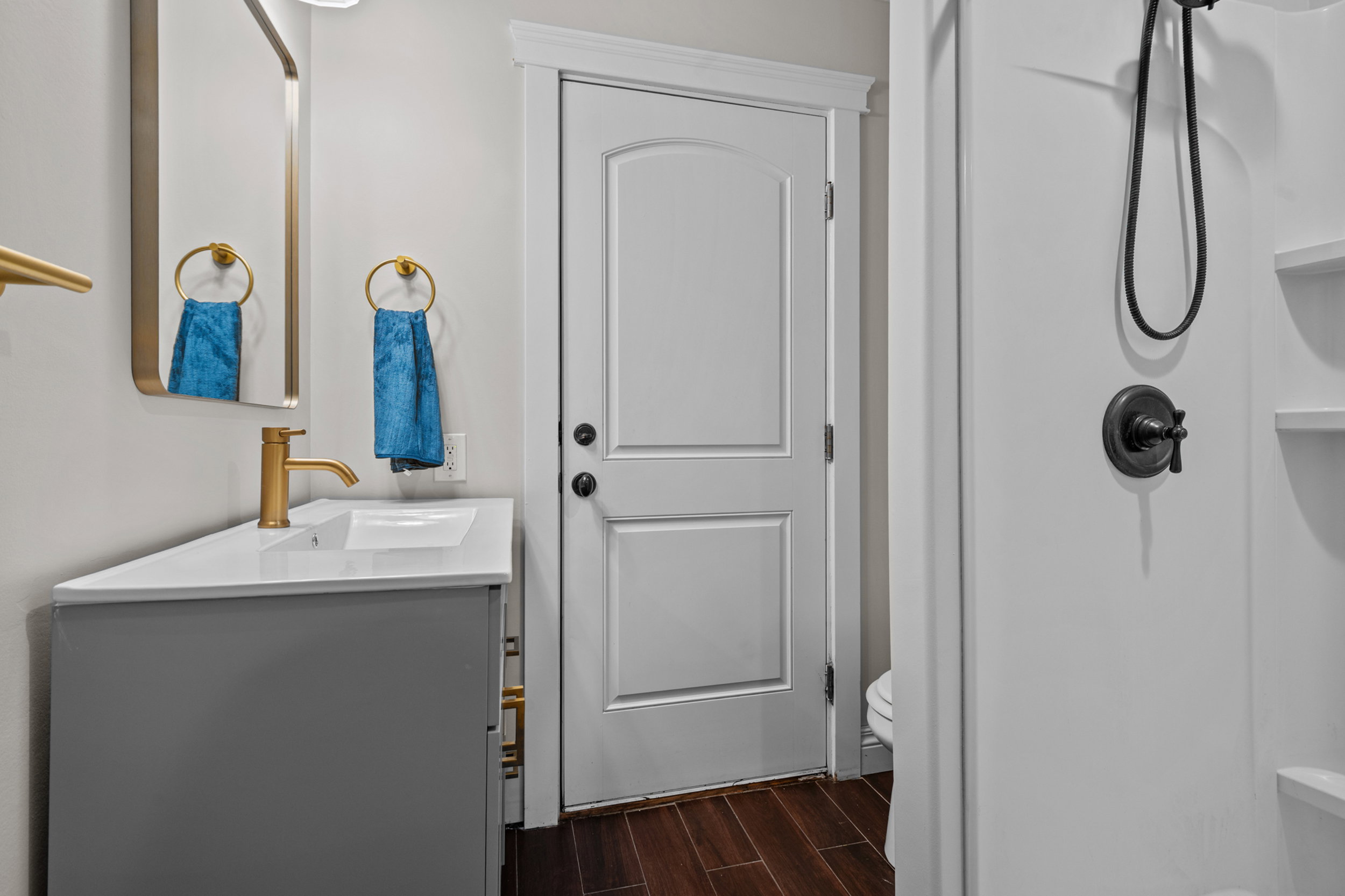 Bathroom featuring a gray vanity with a white countertop and integrated sink, gold-tone faucet, and an exterior door (to backyard)