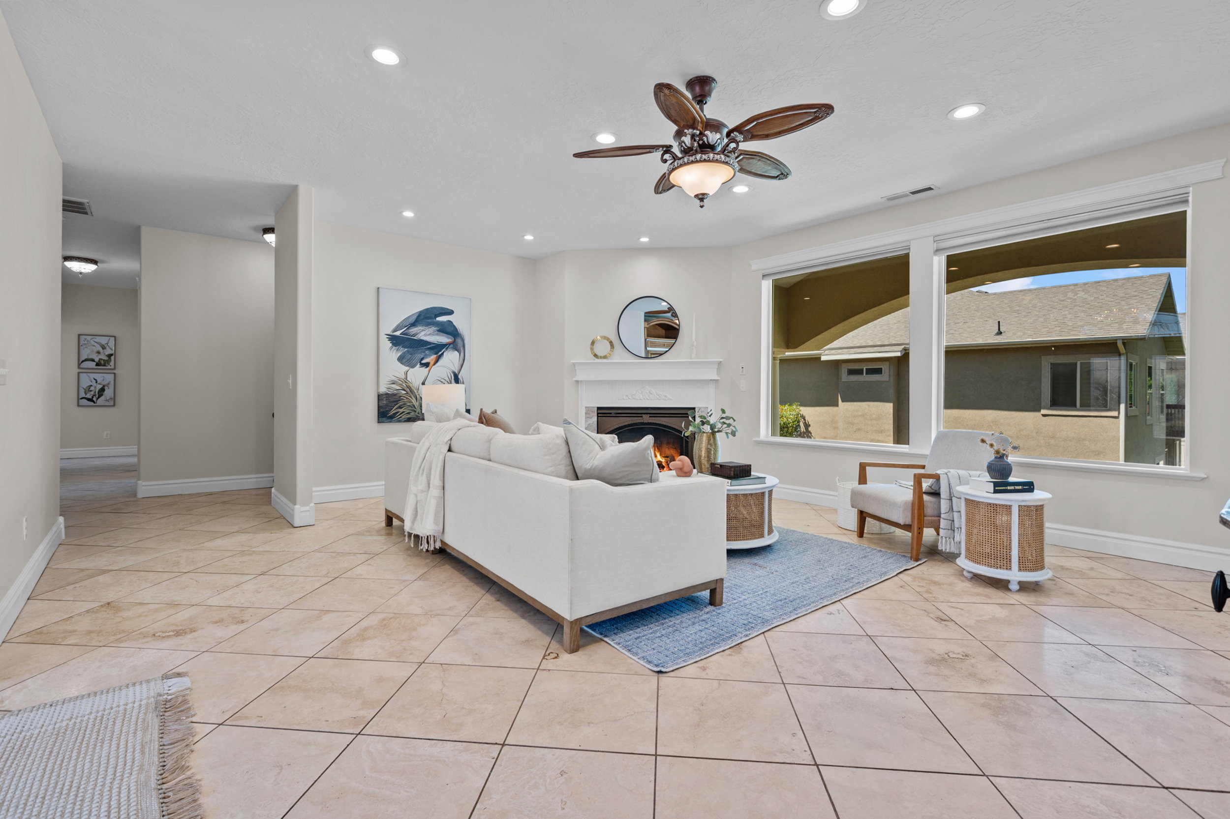 Spacious living area featuring large windows, a fireplace with a white mantel, recessed lighting, a ceiling fan