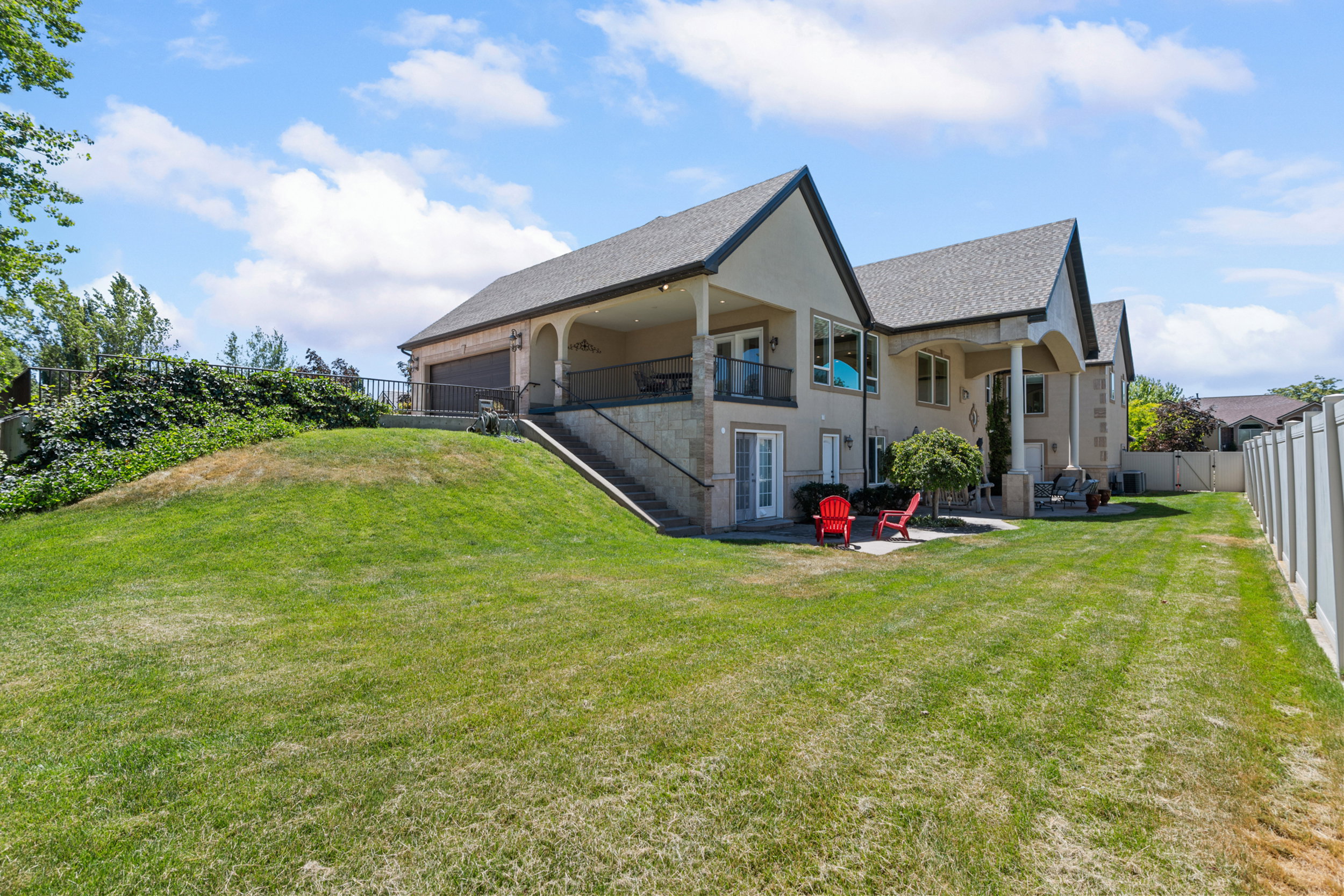 Expansive rear yard featuring a sloped lawn area, mature landscaping, and a privacy fence
