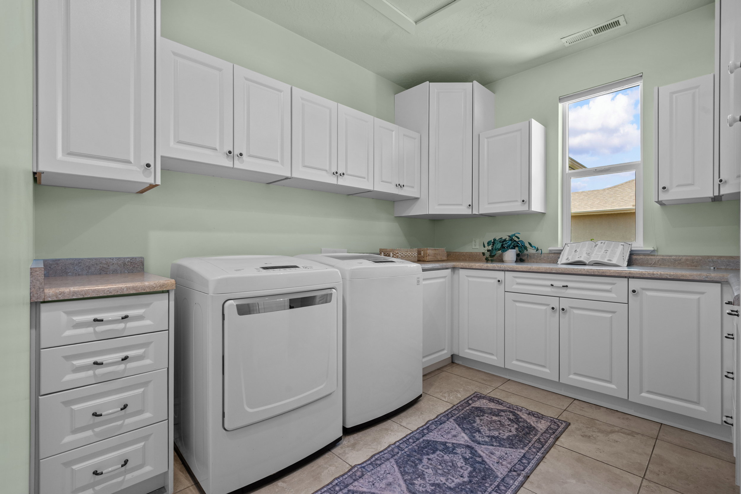 Laundry room featuring extensive white cabinetry, light-toned countertops, and tile flooring. Sink is plumbed next to washer.