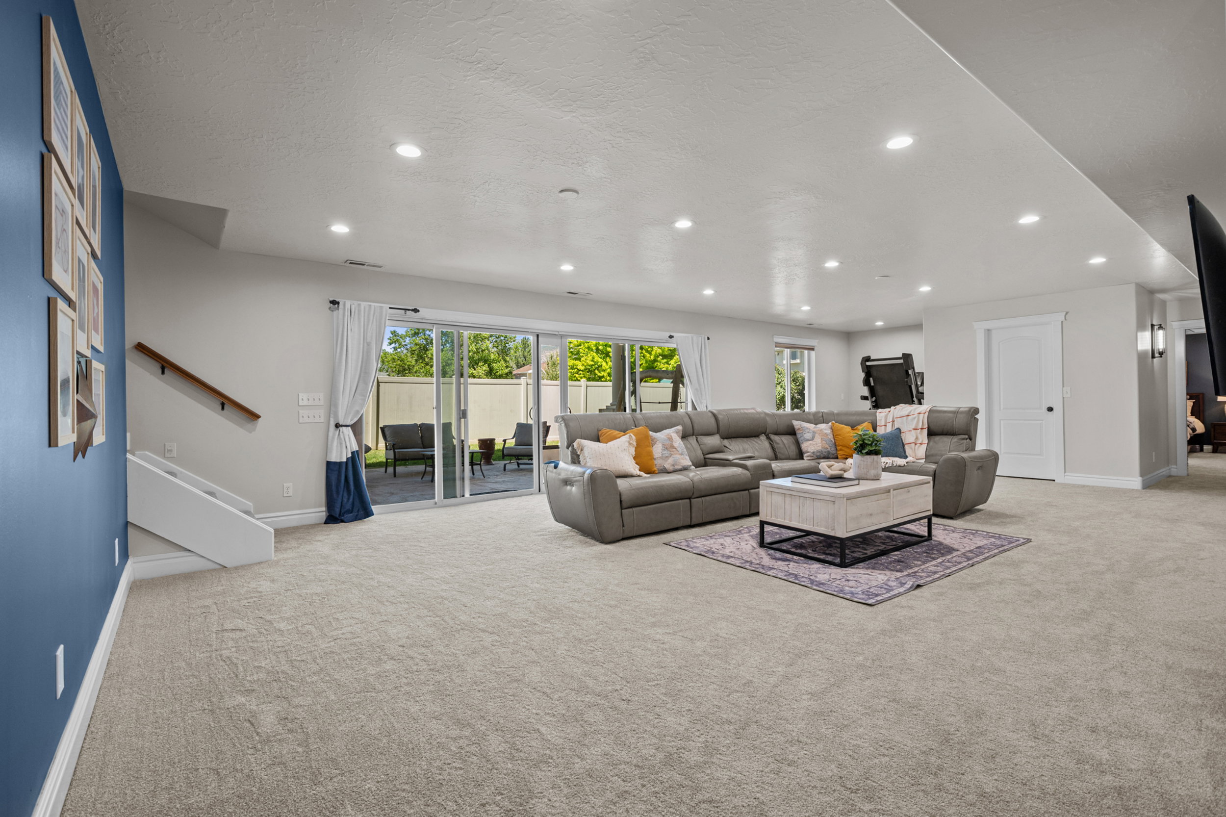 Spacious living area featuring light-toned carpet, recessed lighting, and a sliding glass door providing exterior access
