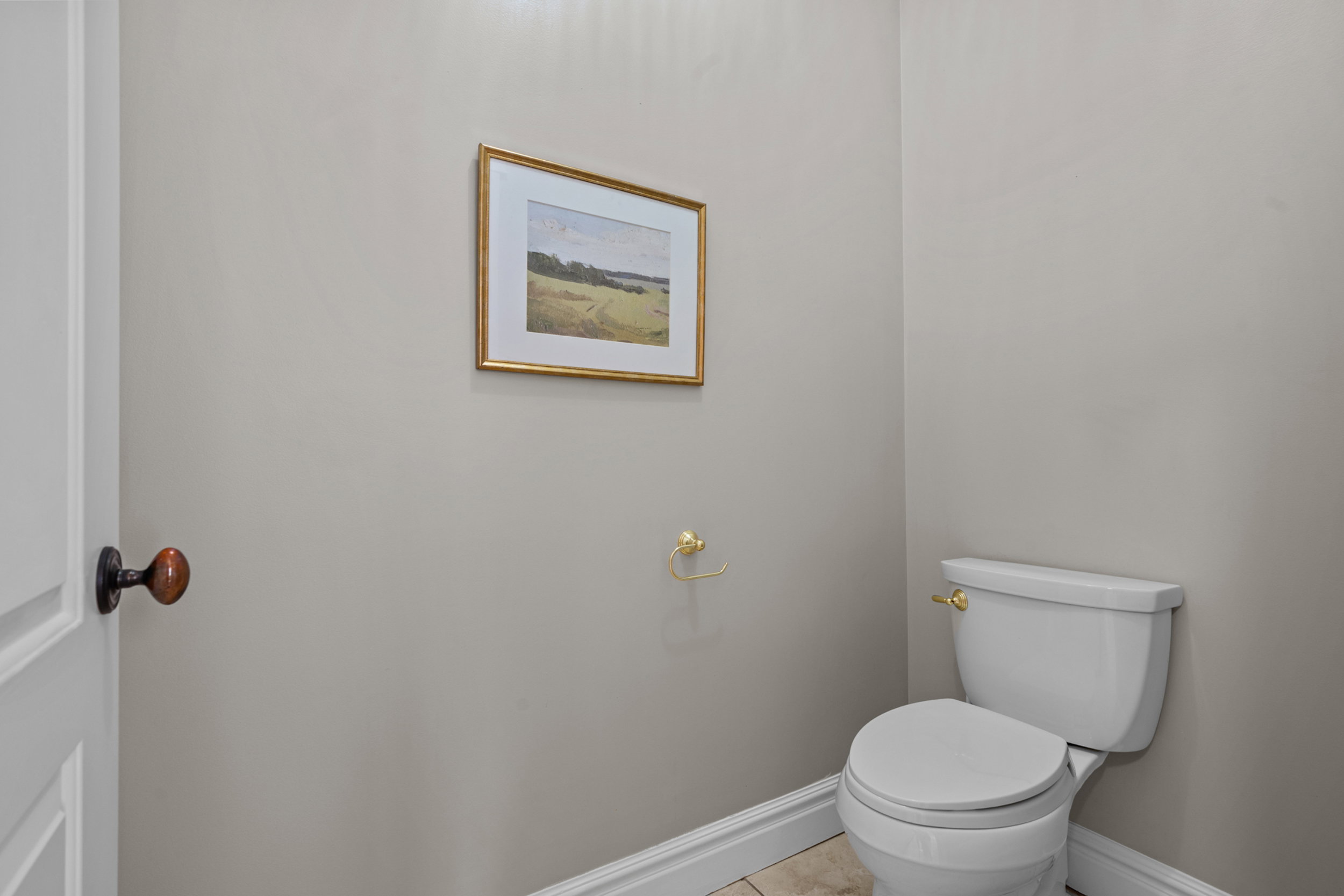 White toilet with gold-tone fixtures, light neutral wall paint, white baseboards, and tile flooring