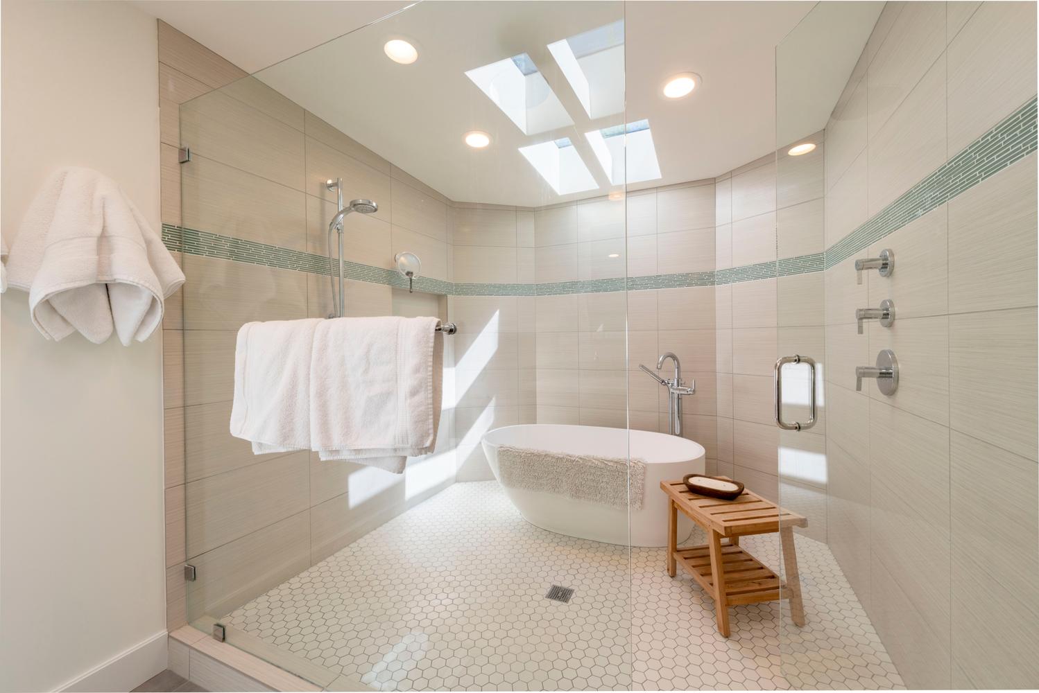 Glass-enclosed shower with a freestanding soaking tub, mosaic accent tile, skylights, recessed lighting, and hexagon floor tile