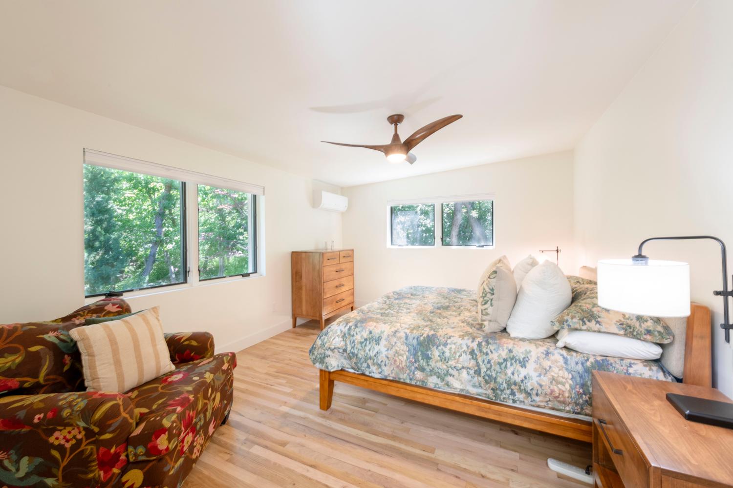 Spacious room featuring wood-finish flooring, two large windows, a mini-split climate control system, a modern ceiling fan with integrated lighting, and neutral wall tones