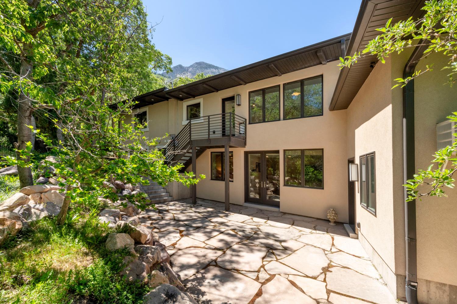 Lower-level exterior featuring a flagstone patio, stucco facade, and a modern balcony with metal railings and exterior stairs
