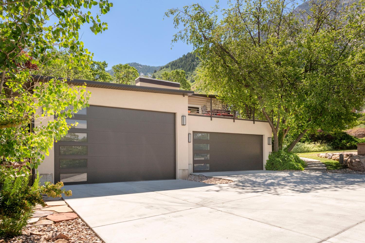 Contemporary exterior with dual garage doors featuring frosted glass panels, an upper-level balcony with metal railings, and a concrete driveway