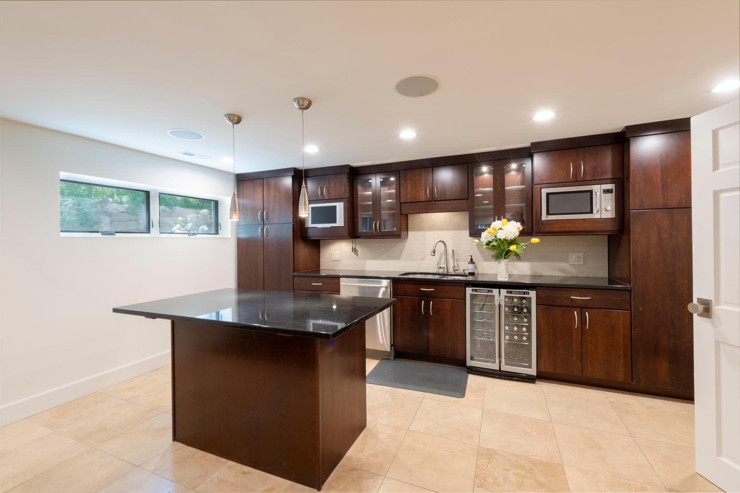 Kitchenette featuring dark wood cabinetry, a central island with a black countertop, stainless steel appliances, and tile flooring
