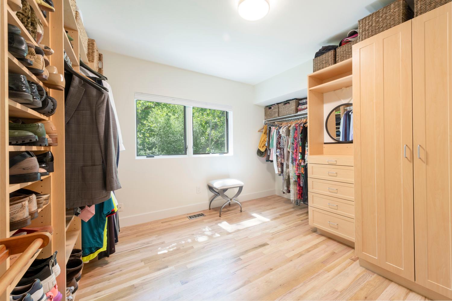 Spacious walk-in closet featuring extensive built-in shelving, wood-finish flooring, and a large window providing natural illumination
