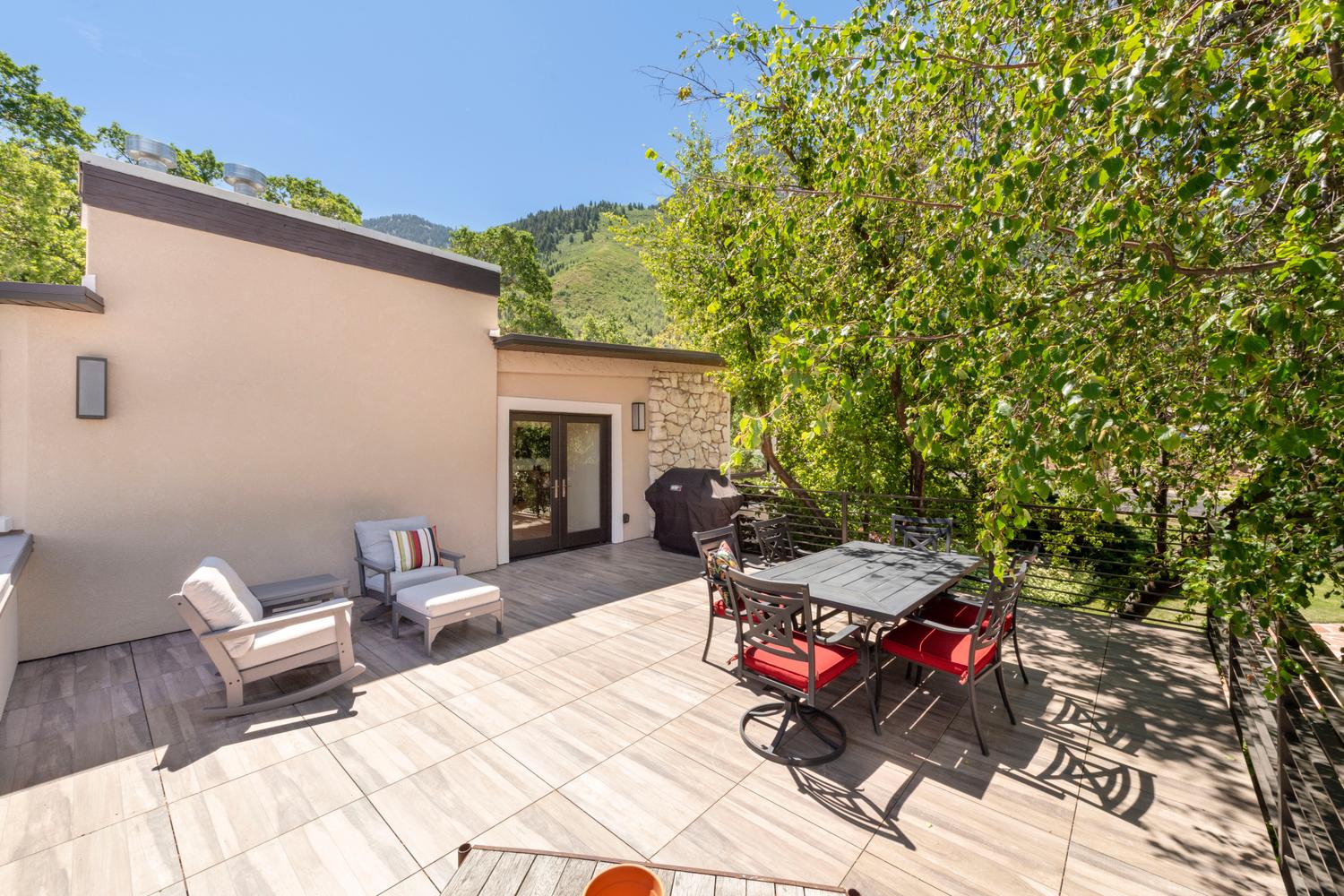 Expansive outdoor deck featuring large format tile flooring and surrounding mature greenery