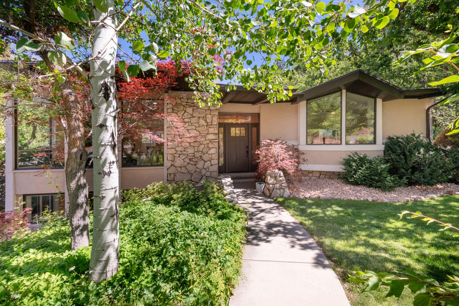 Contemporary-style residence featuring a stone facade accent, large picture windows, and a concrete pathway leading to the entry