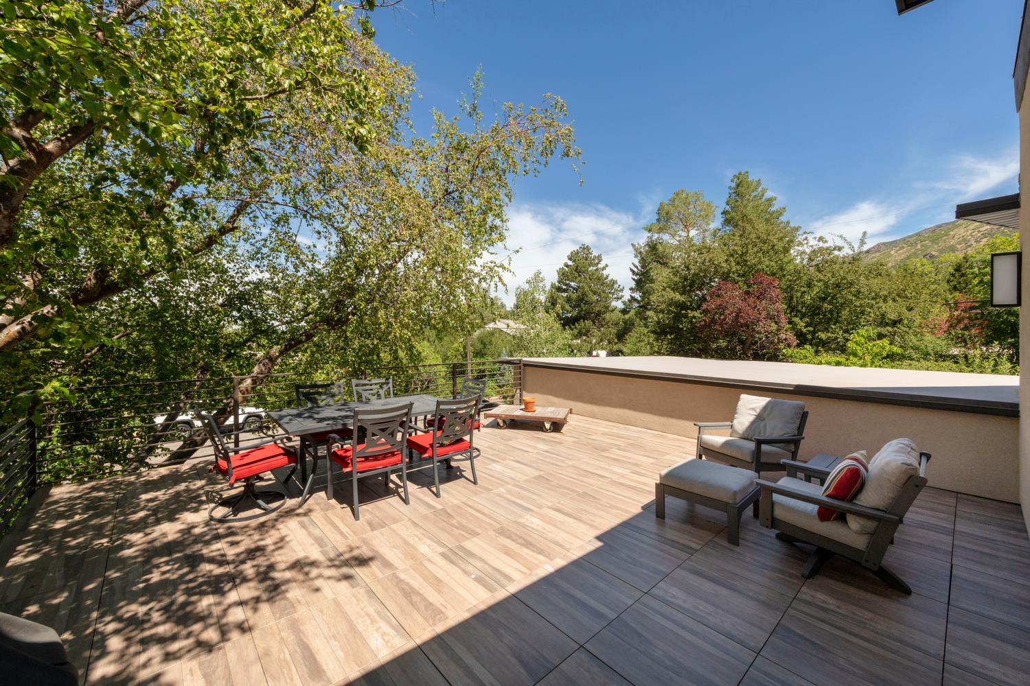 Expansive outdoor deck featuring wood-finish flooring, a contemporary exterior wall, and surrounding mature trees