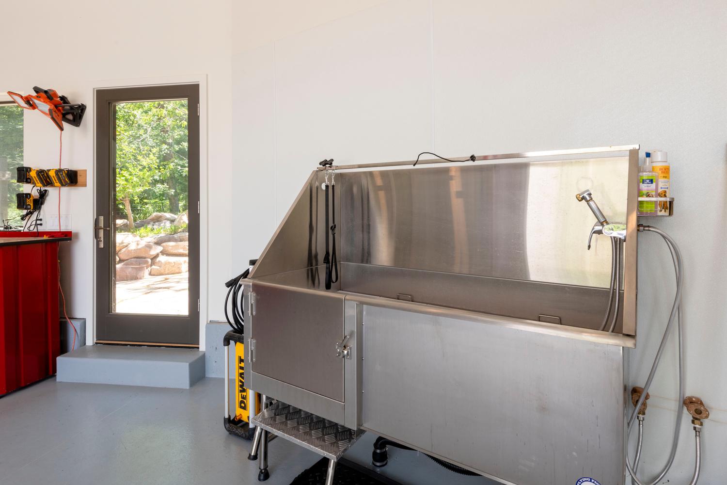 Utility area featuring a stainless steel wash basin with an integrated sprayer, a wall-mounted glass panel door, and gray concrete flooring
