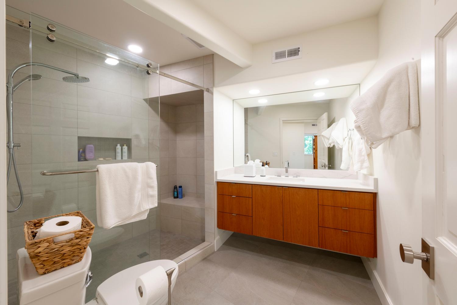 Contemporary bathroom featuring a frameless glass shower enclosure, rainfall showerhead, integrated shower niche, floating vanity with dual sinks, and a quartz countertop
